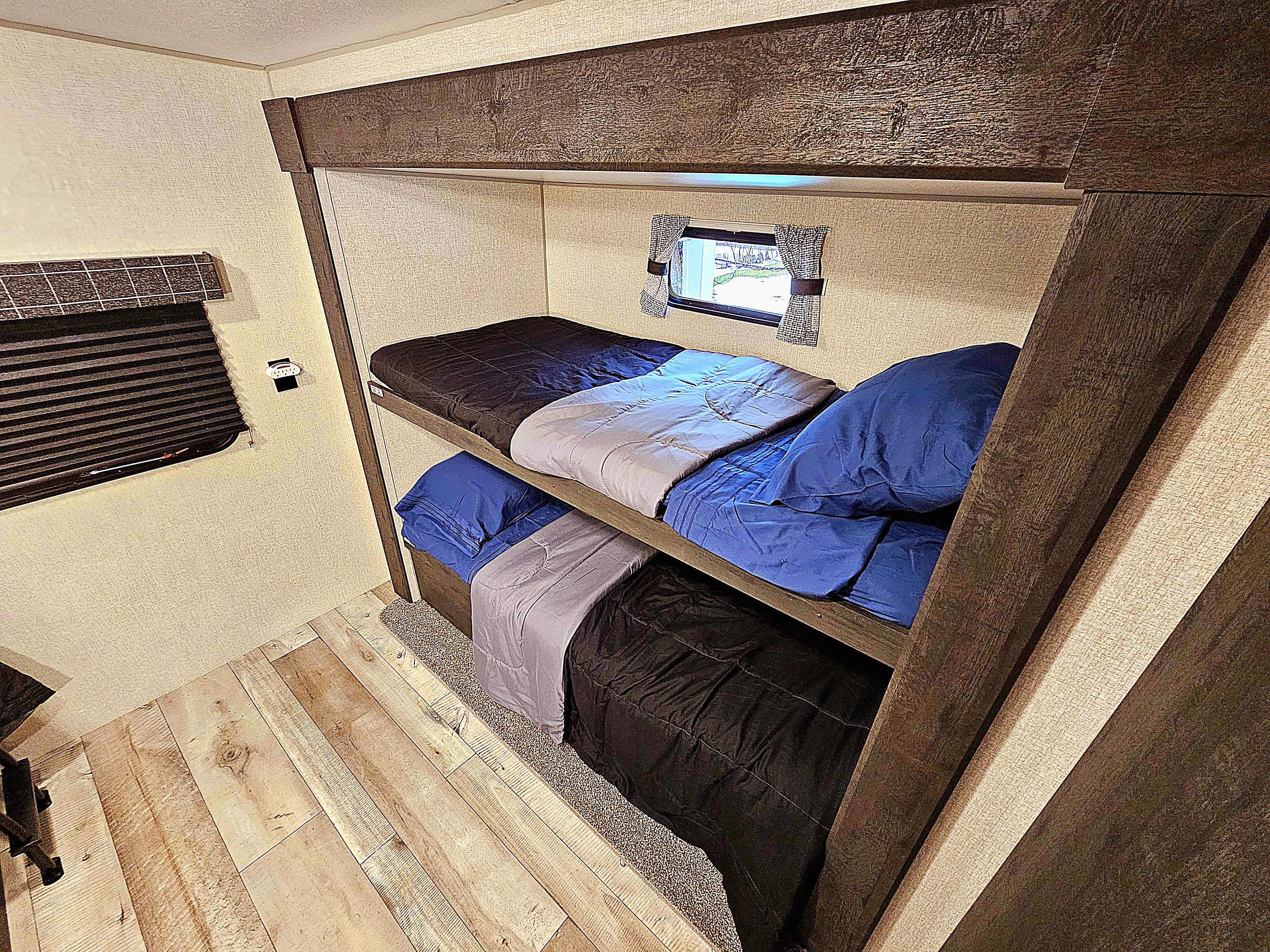 Comfortable bunk beds in an RV rental, perfect for family camping trips. Features wood accents, window, and cozy bedding.. KZ 312 Bunk House 2022