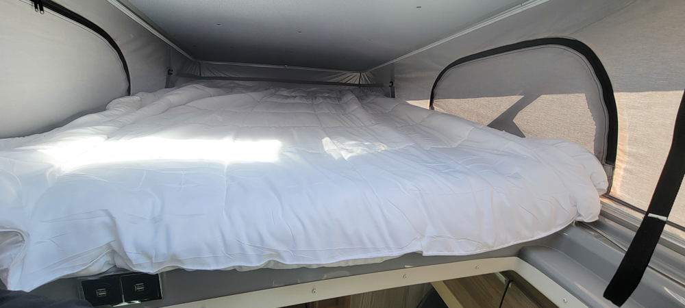 Bright and cozy pop-top bed with white comforter inside an RV rental, ready for comfortable travel adventures.. Thor Motor Coach Sequence 2023