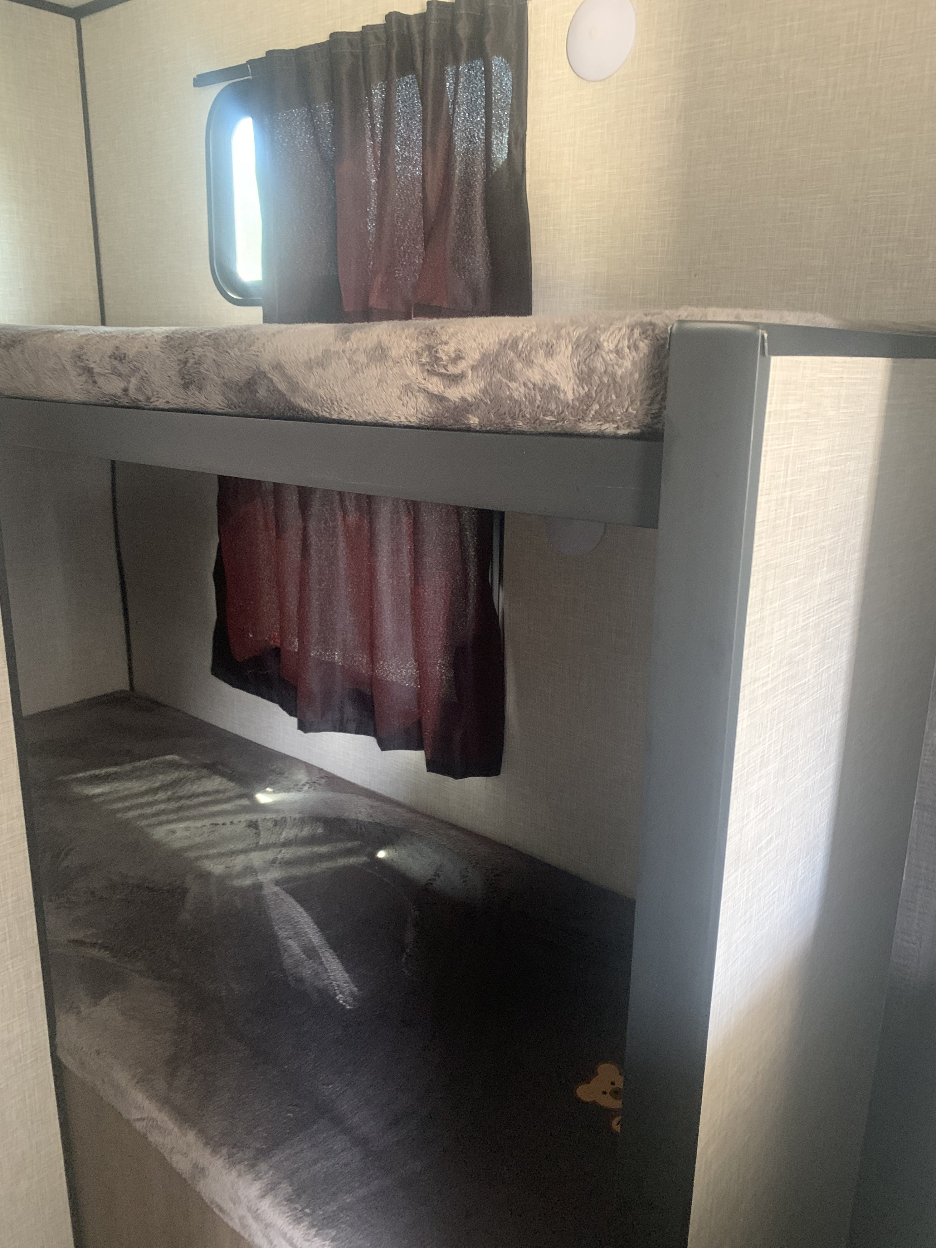 Cozy bunk beds in an RV rental: a light fluffy top mattress, a dark bottom mattress, and a window with curtains.. Highland Ridge Open Range 2023