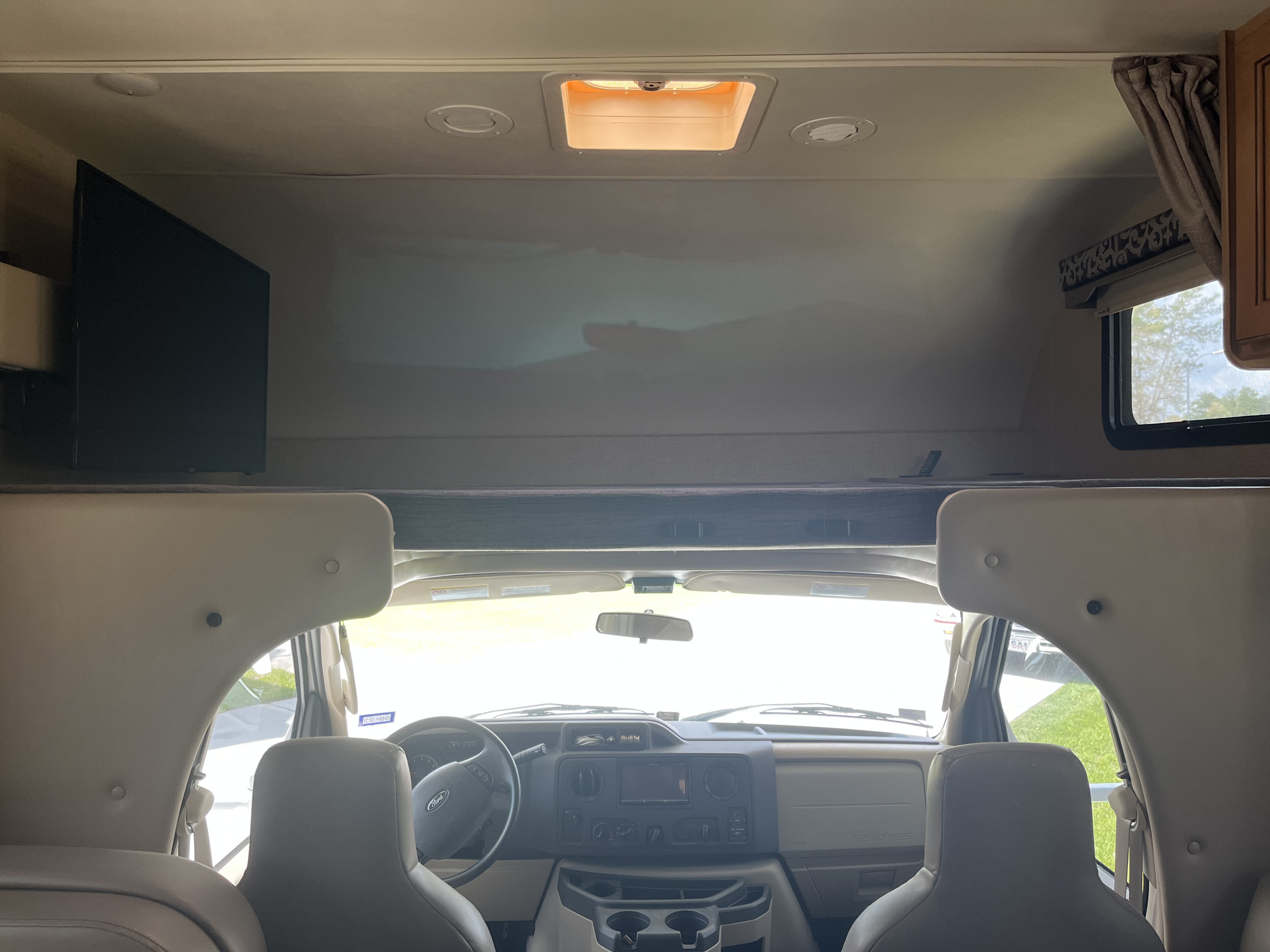 Inside a spacious RV rental, featuring the front cab, dashboard, steering wheel, TV, and overhead bunk.. Thor Four Winds 2017