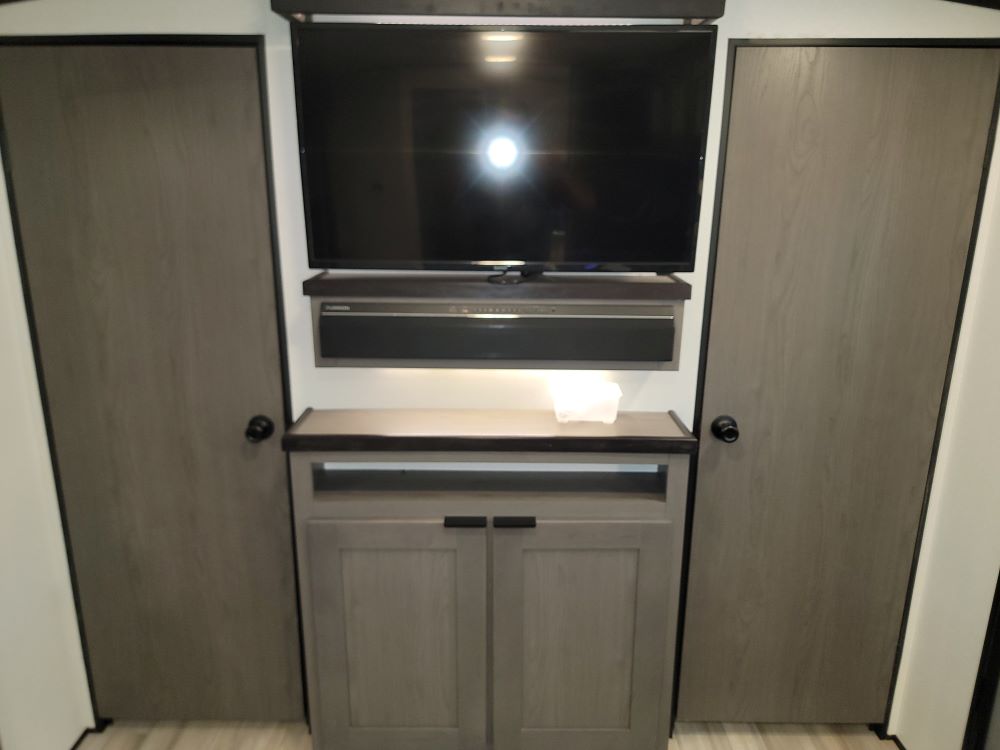 Inside an RV rental: a modern entertainment center with TV, soundbar, counter space, and cabinets flanked by two doors.. Cruiser RV MPG Ultra Lite 2021