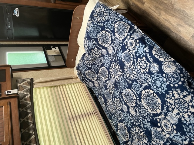 RV rental interior featuring a compact fridge, window, and a bed with a vibrant blue and white patterned blanket. Comfortable amenities.. Jayco White Hawk 2017