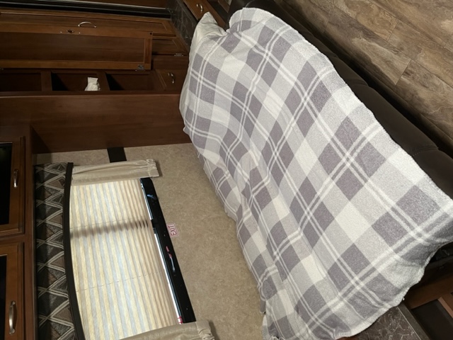 Cozy RV rental interior with a plaid blanket on the sofa, wooden cabinets, and window with an exit sign.. Jayco White Hawk 2017