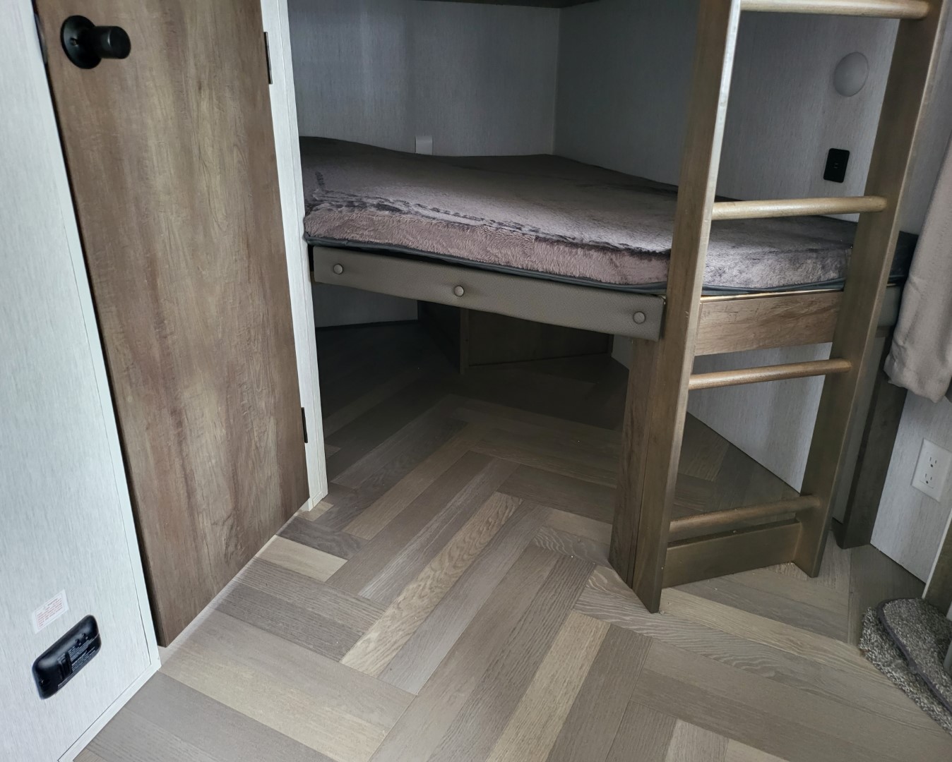 RV rental bunk beds with a wooden ladder, soft mattress, and modern herringbone flooring in a compact interior.. Forest River Salem 2022