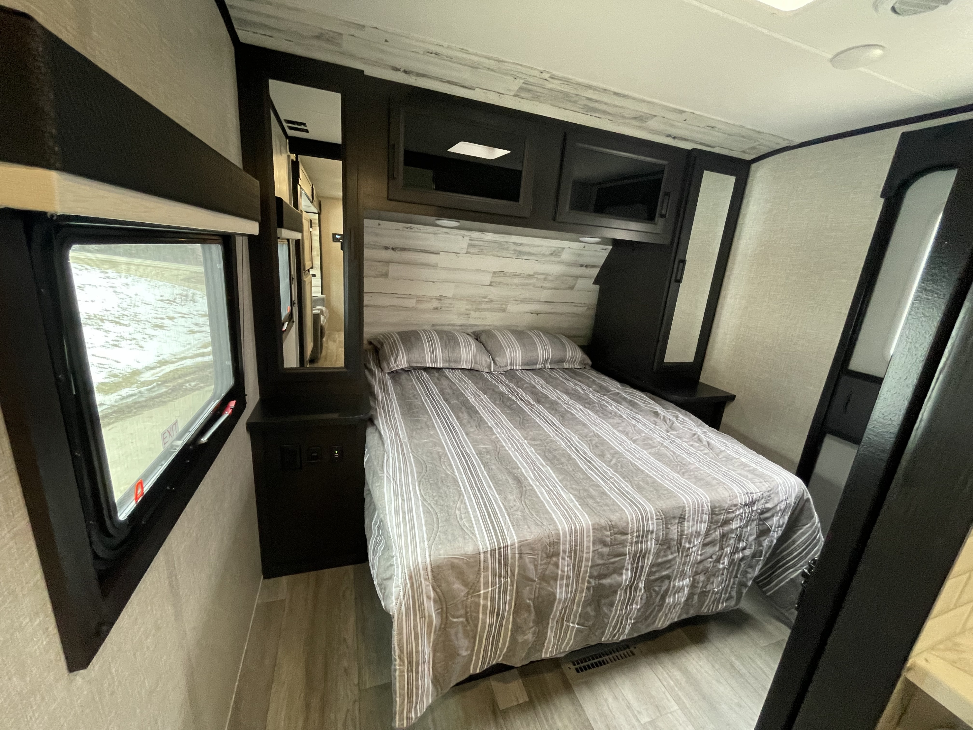 Comfortable RV rental bedroom with striped bedding, overhead cabinets, and a window view, offering a cozy retreat.. Jayco Jay Feather 2022