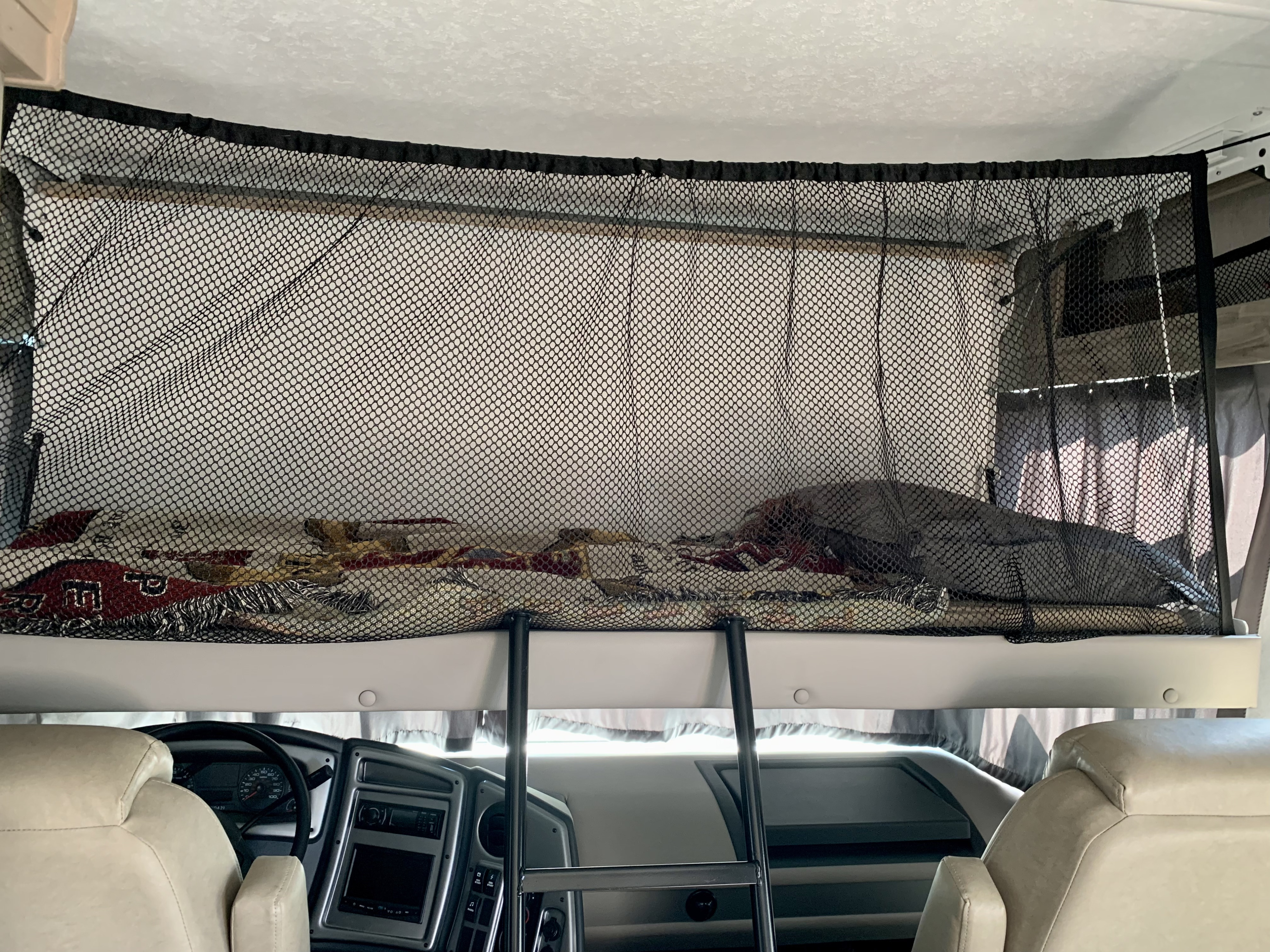 Overhead bunk with safety net, ladder, and cozy bedding in an RV rental. Cockpit dashboard visible below.. Forest River Coachmen Pursuit 2020