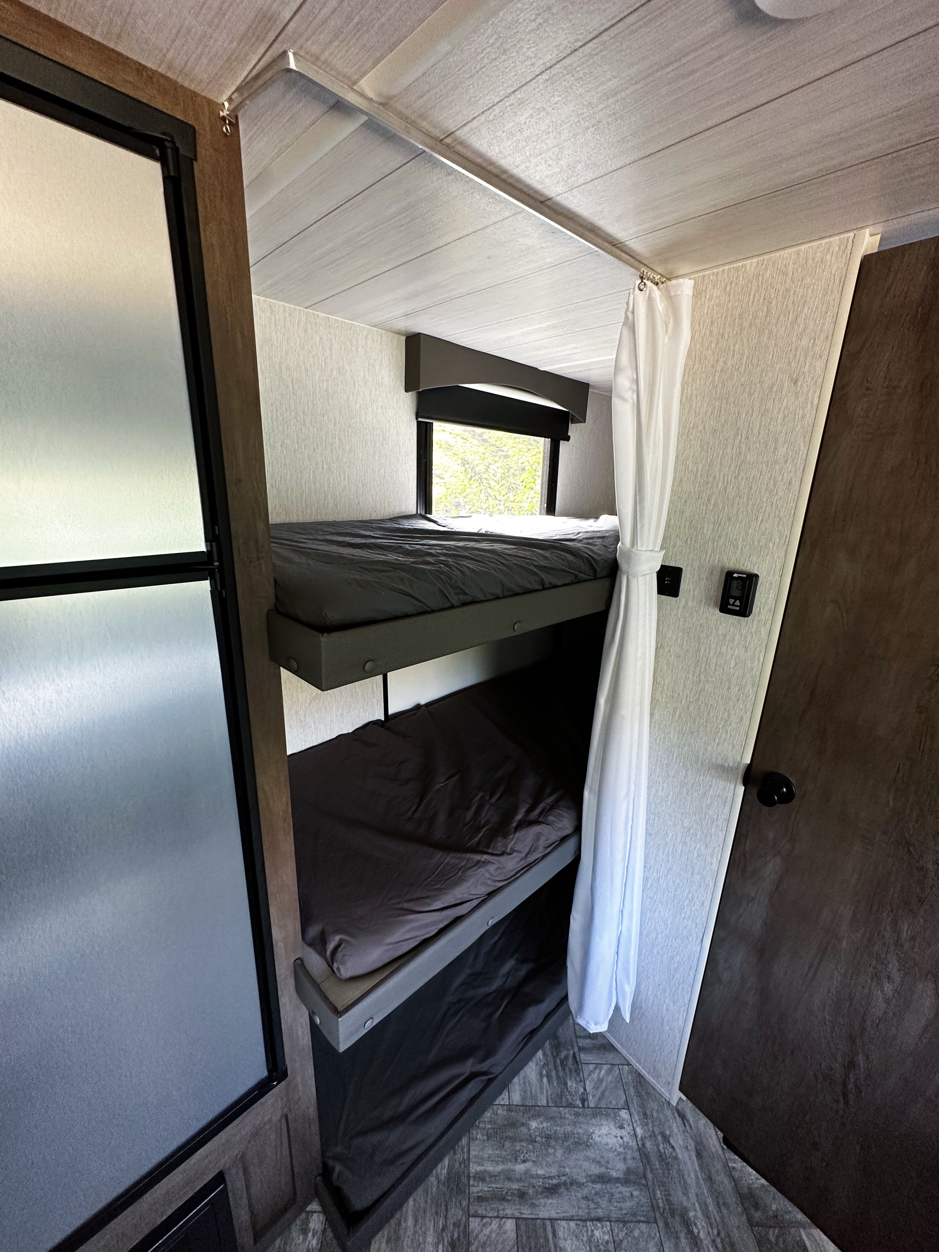 RV rental interior: cozy bunk beds with window, privacy curtain, and adjacent refrigerator. Compact sleeping area.. Forest River Evo 2022