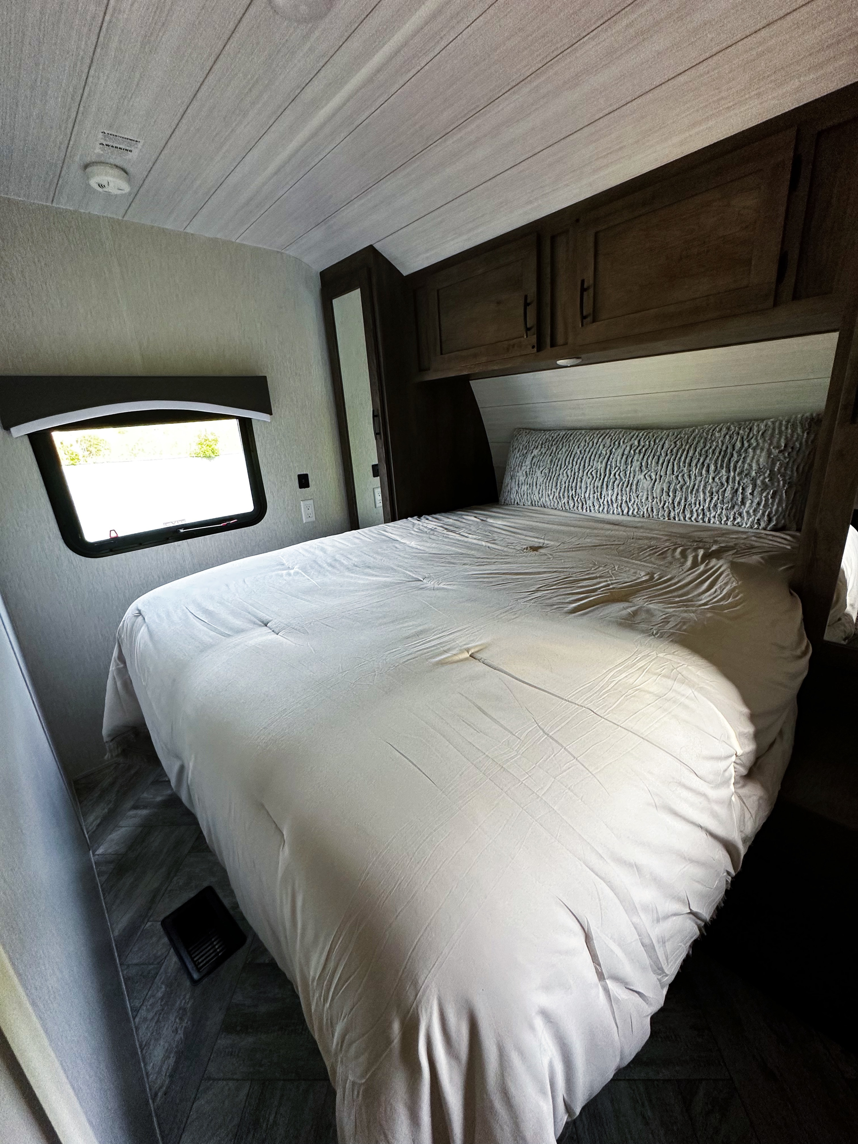 Cozy RV rental bedroom with a large bed, overhead cabinets, a window, and a slatted ceiling.. Forest River Evo 2022