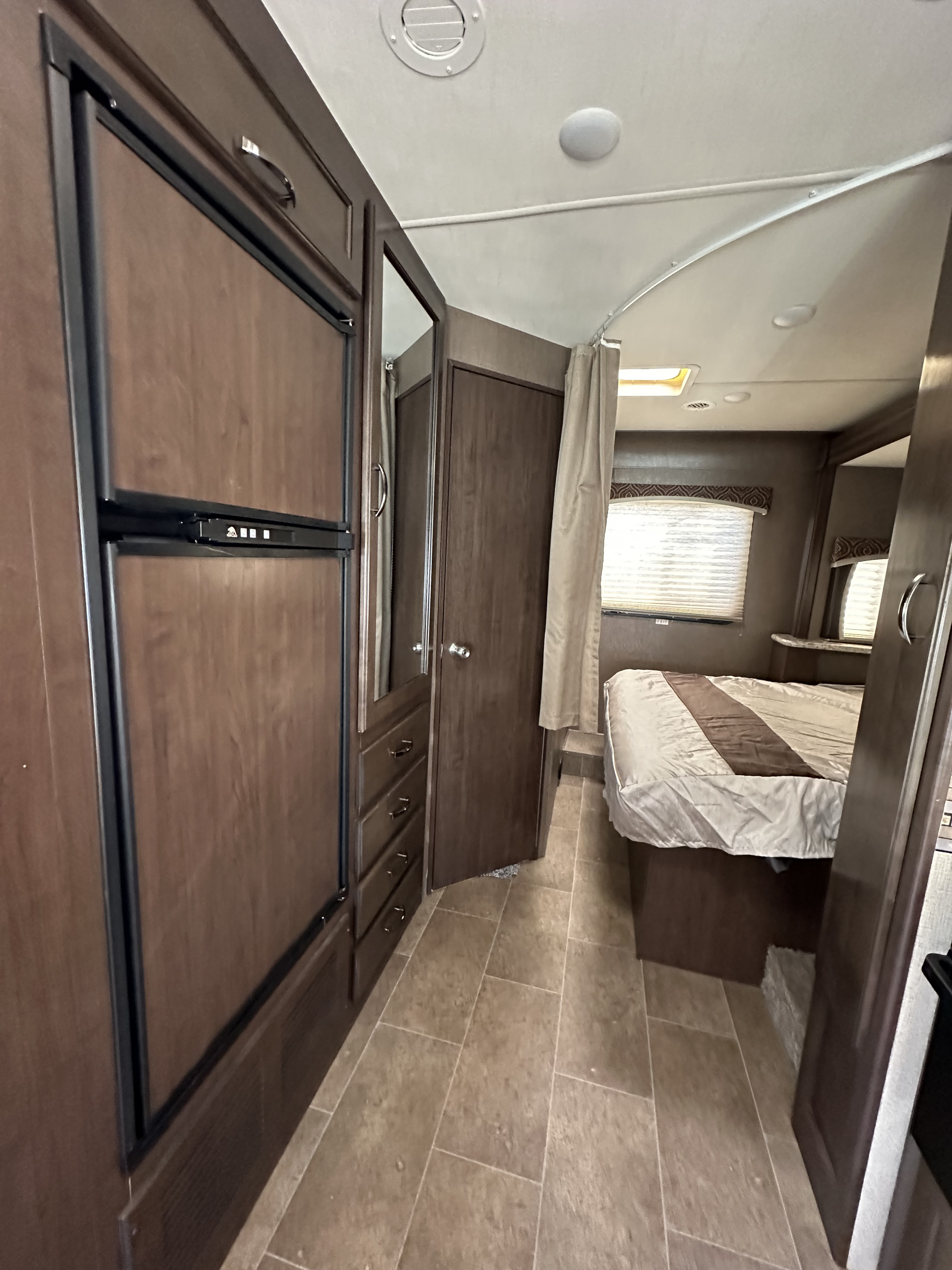RV rental interior featuring a cozy bedroom area with a bed and window, alongside a kitchenette with fridge and storage cabinets.. Thor Chateau 2018