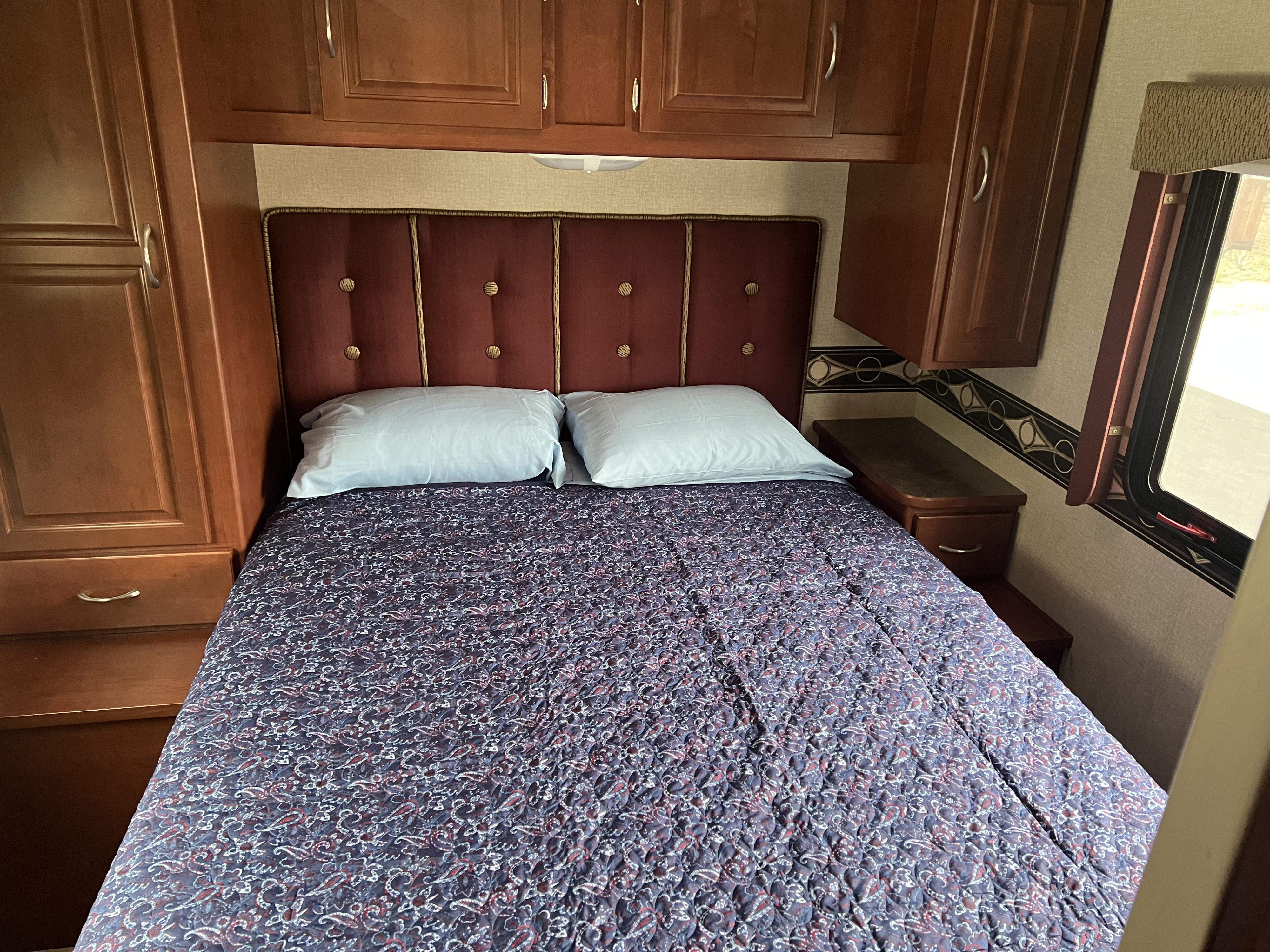 Cozy RV rental bedroom features a comfortable bed with a patterned comforter, padded headboard, and ample storage cabinets.. Winnebago Minnie Winnie 2015