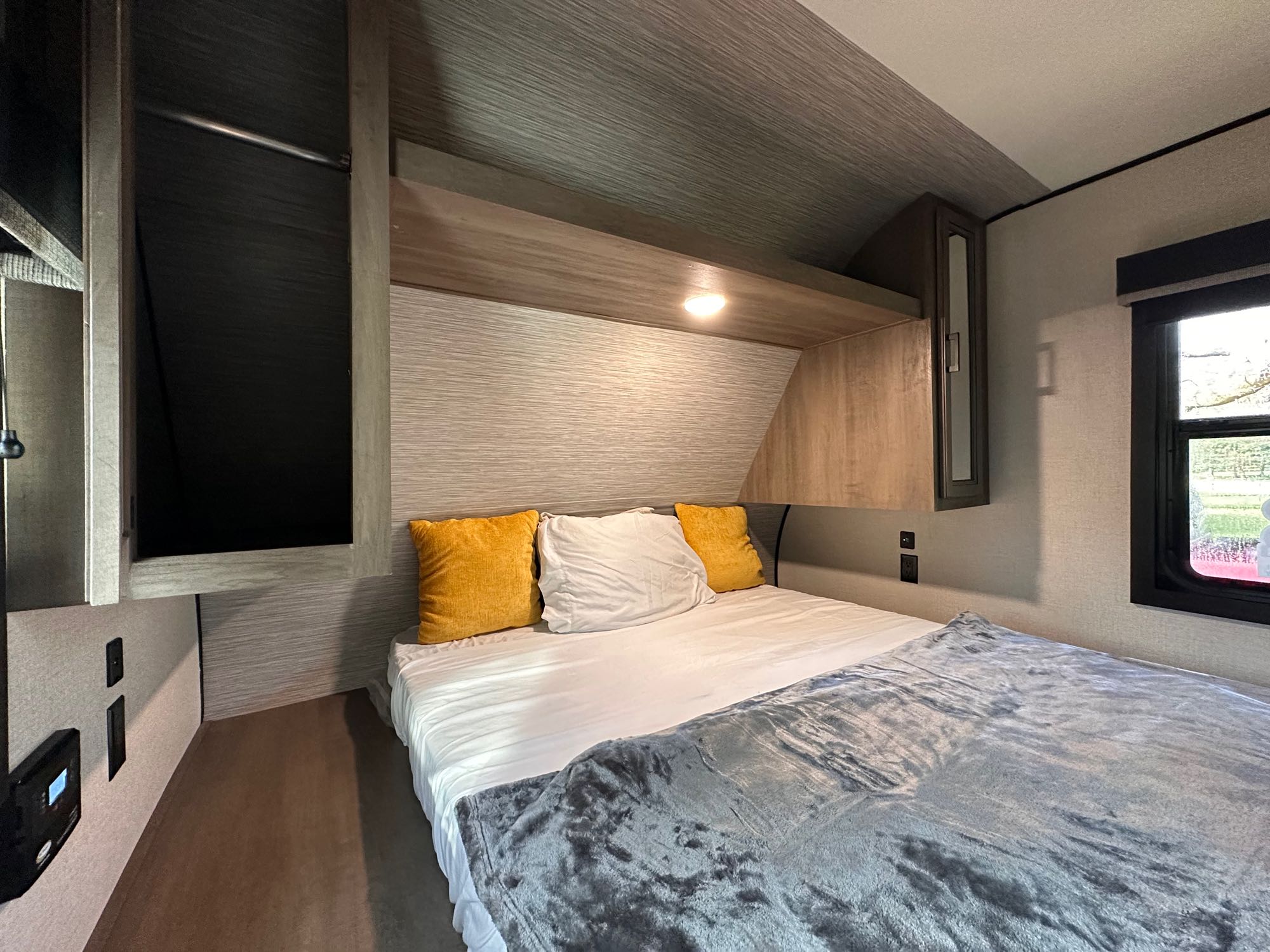 RV rental bedroom with comfortable bed, yellow and white pillows, overhead storage, closet space, and a window.. Highland Ridge RV Olympia 2022