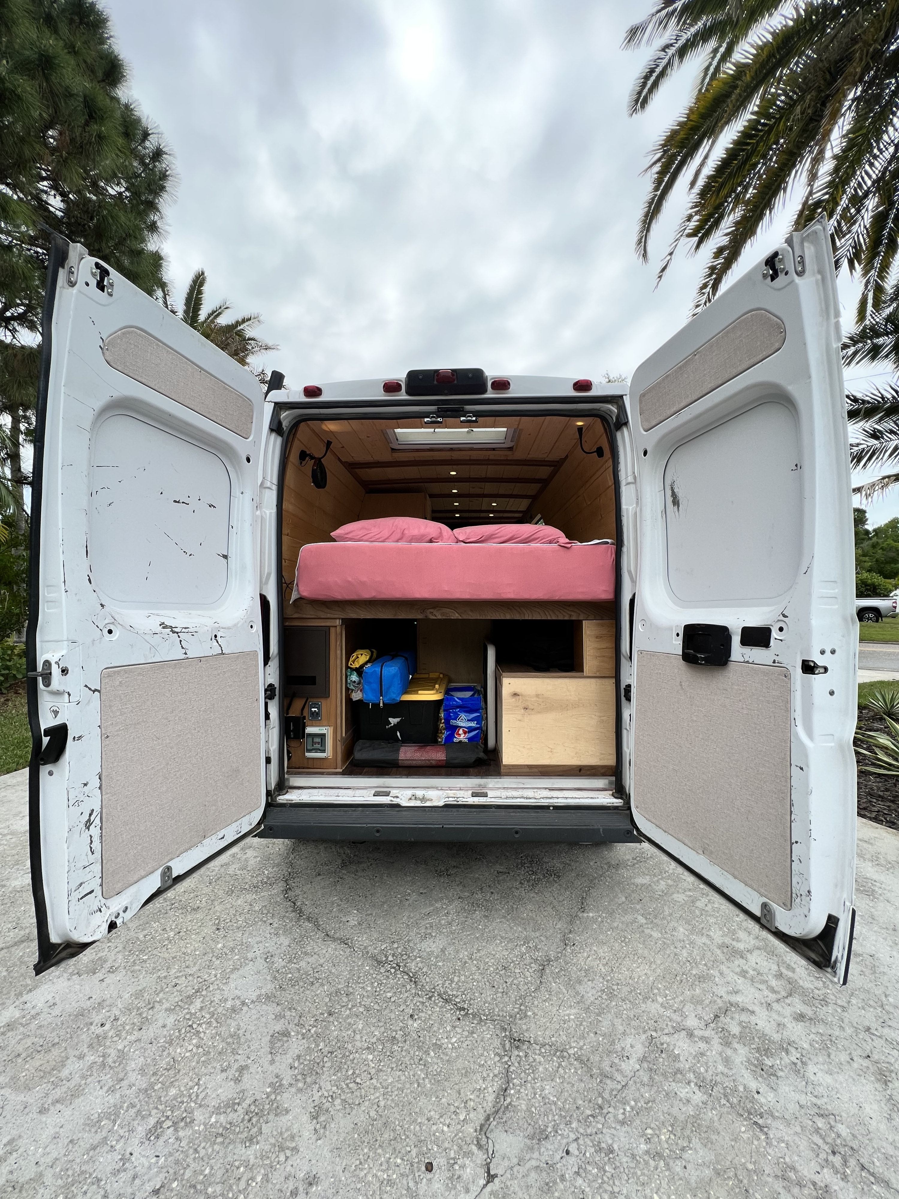 Inside a white camper van: comfortable pink bed, wood interior, and storage space. Ideal RV rental for your next adventure.. Dodge Ram Promaster 2500 2018