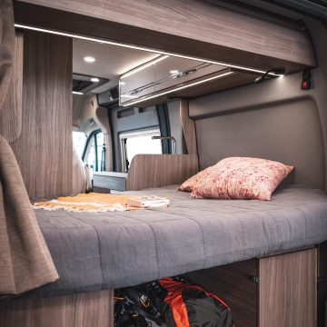 Explore a comfortable RV rental campervan interior: a cozy bed with modern lighting, ready for your next adventure. Under-bed storage visible.. Ranger R540 2023