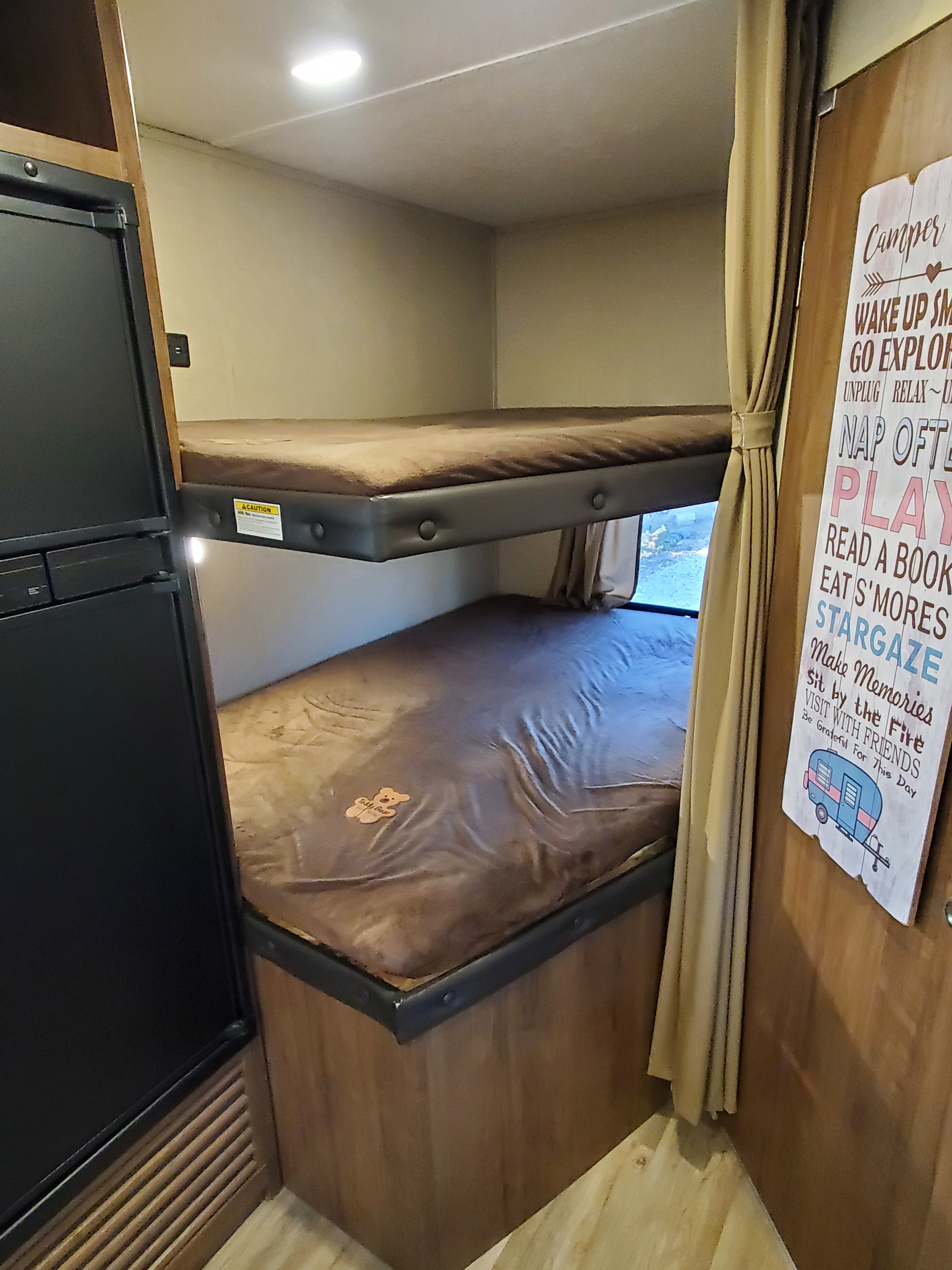 Cozy RV rental interior featuring stacked bunk beds, a refrigerator, and a decorative sign with fun camping phrases.. Aspen Trail Other 2017
