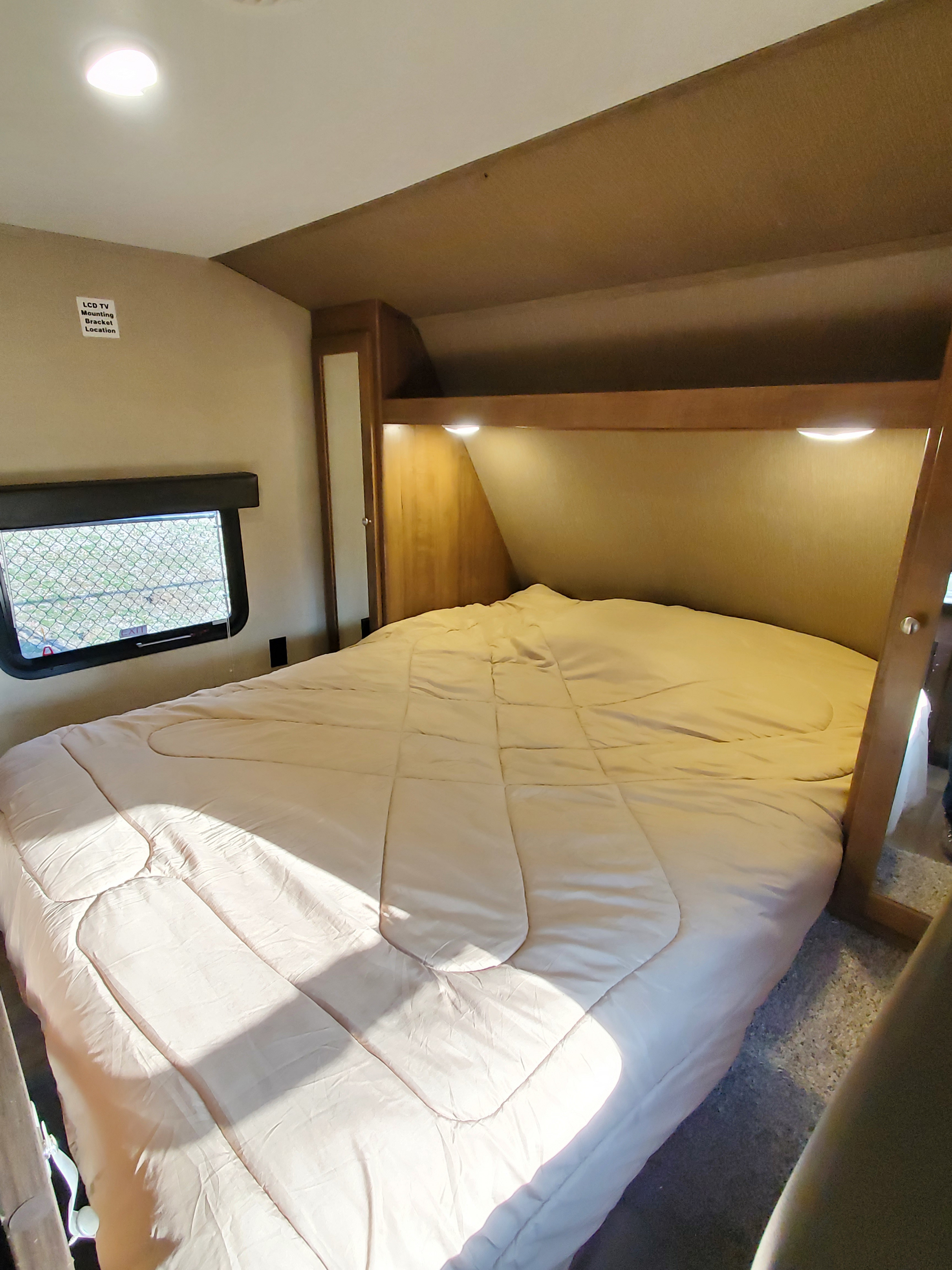 Cozy RV rental bedroom with a large bed, window, built-in storage, and TV mounting location info on the wall.. Aspen Trail Other 2017