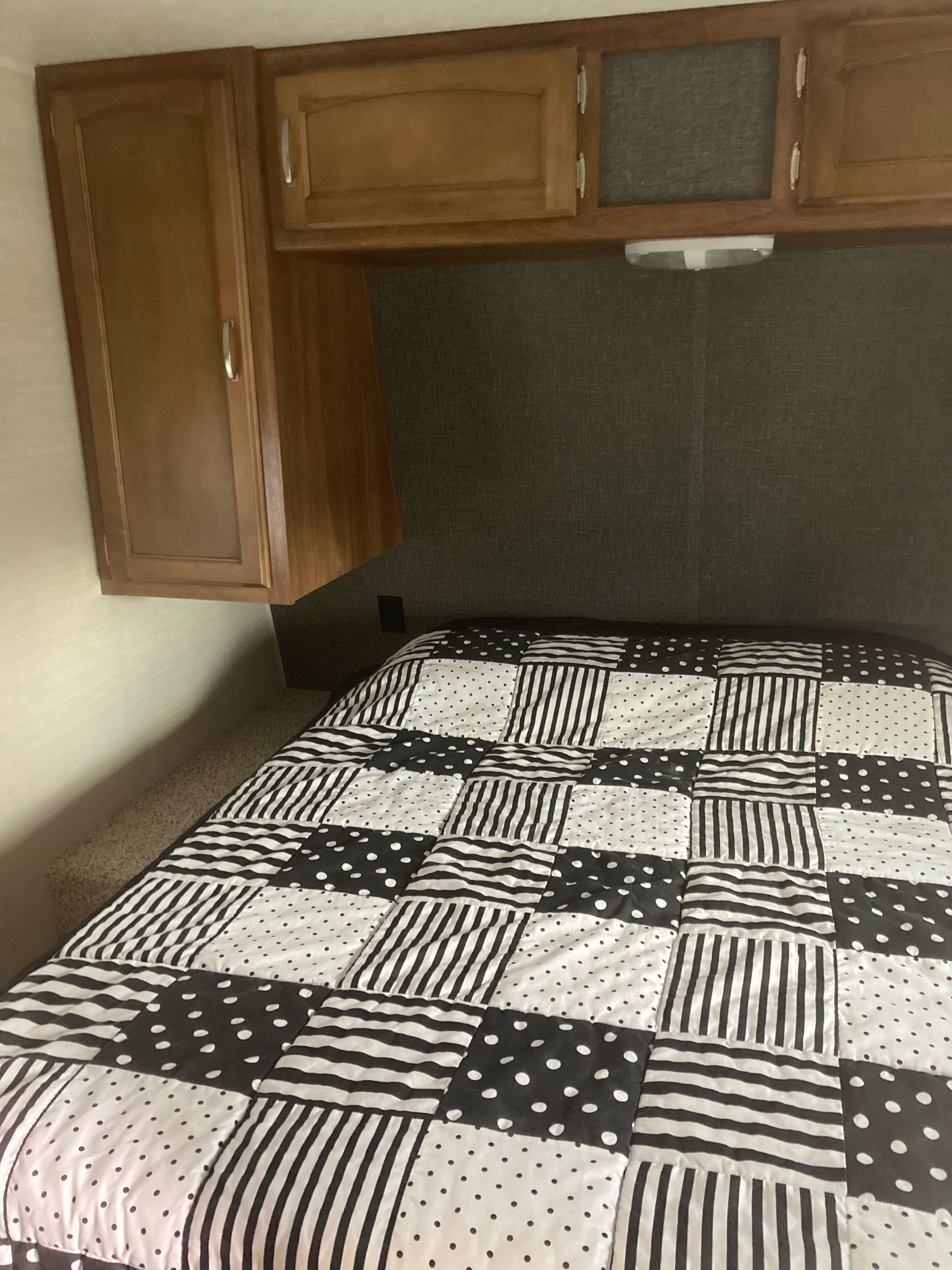 Inside an RV rental: cozy bedroom with a patterned black/white quilt on the bed & overhead storage cabinets.. Keystone RV Summerland 2015