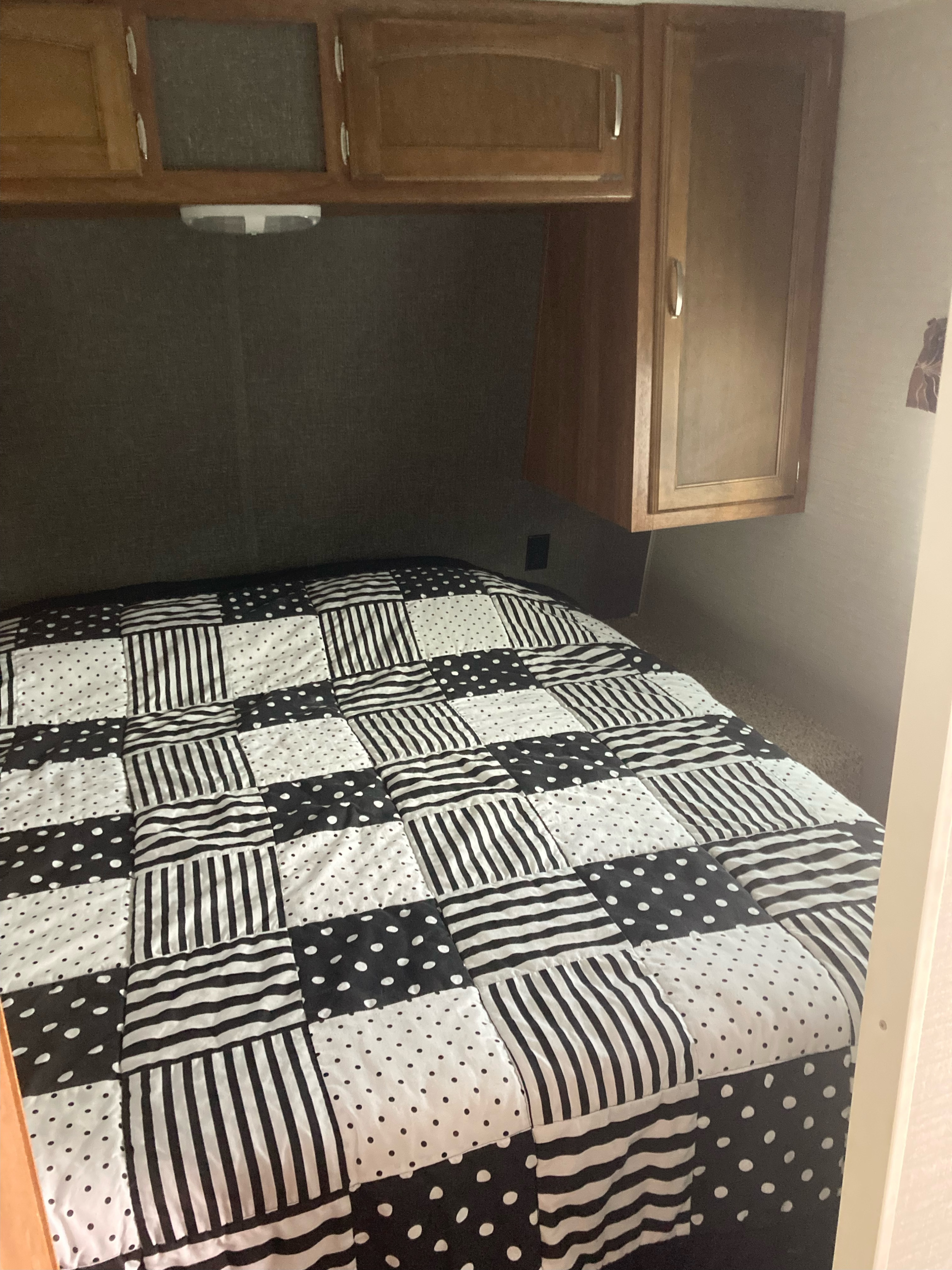 RV rental bedroom featuring a bed with a black & white patterned quilt, overhead cabinets, and a built-in light fixture.. Keystone RV Summerland 2015