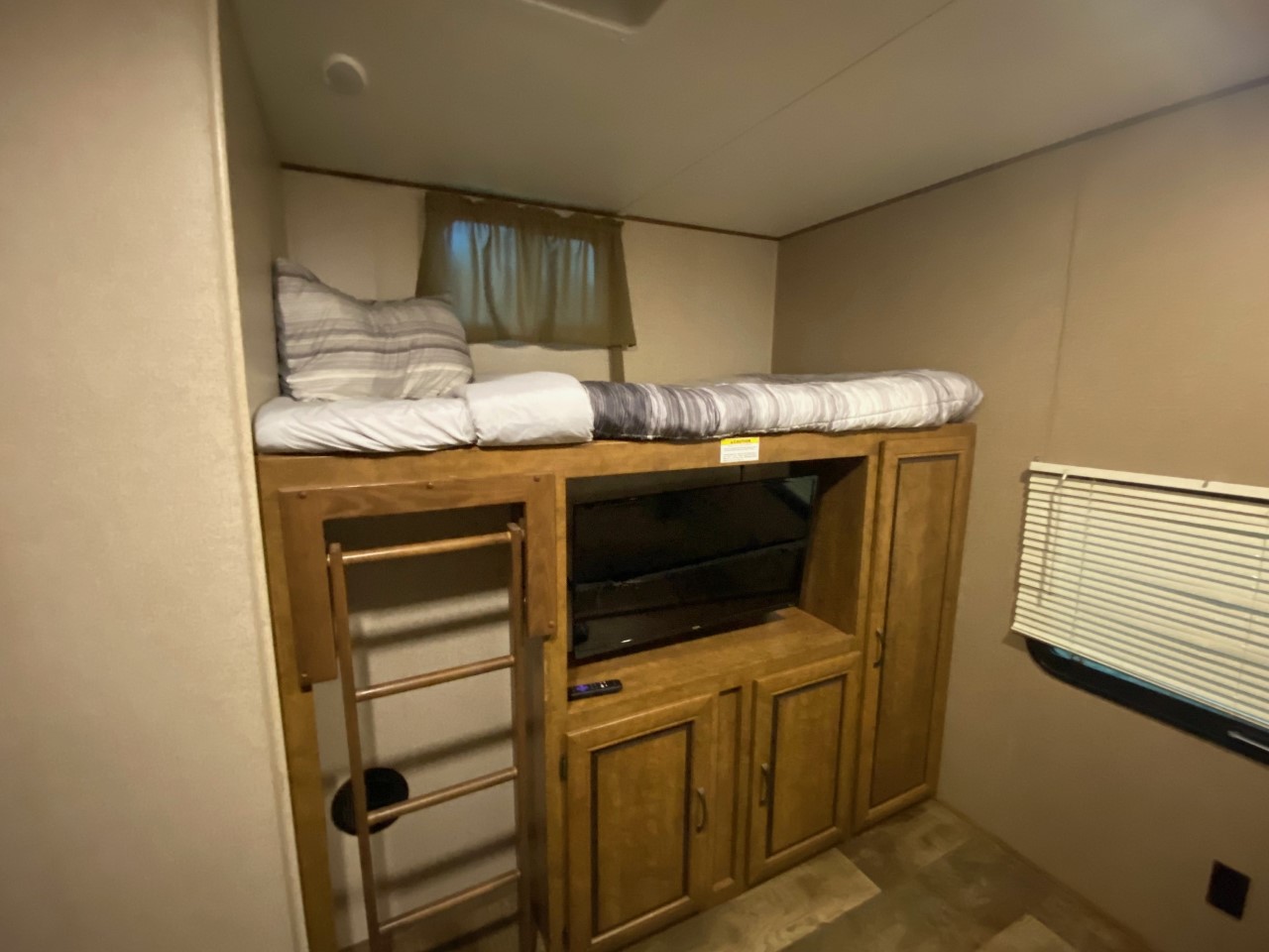 Cozy RV rental interior featuring a bunk bed, ladder, and a TV integrated into wooden cabinetry. A compact sleeping and entertainment space.. Crossroads RV Zinger 2018