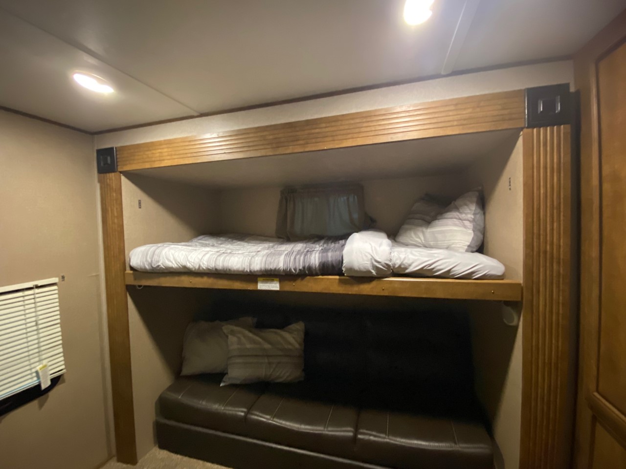 This RV rental interior shows wooden bunk beds, with an upper bed and a lower convertible sofa.. Crossroads RV Zinger 2018