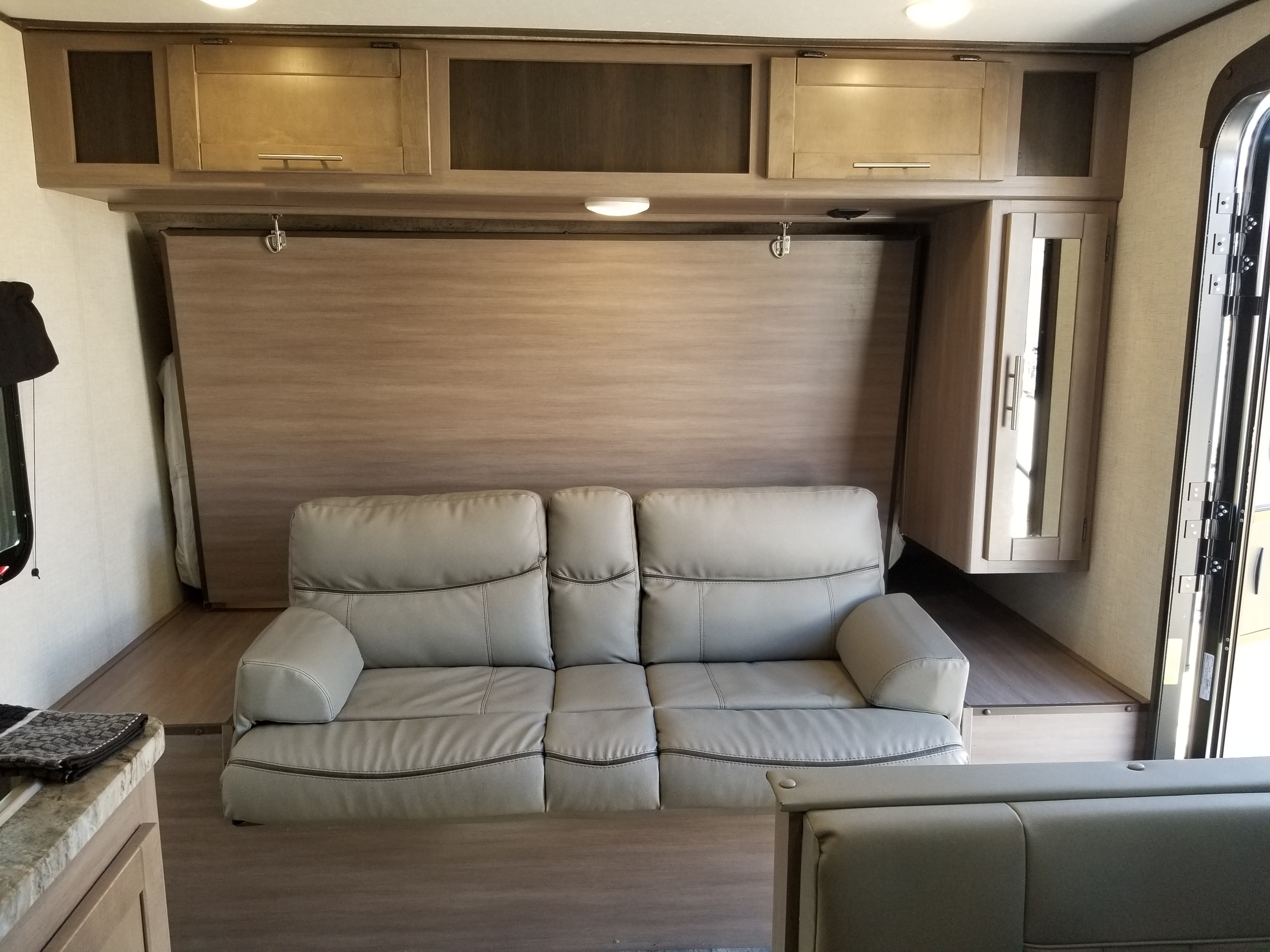 RV rental interior with a light-colored reclining sofa, fold-up Murphy bed, and storage cabinets. A cozy, functional living space.. Crossroads RV Sunset Trail Super Lite 2021