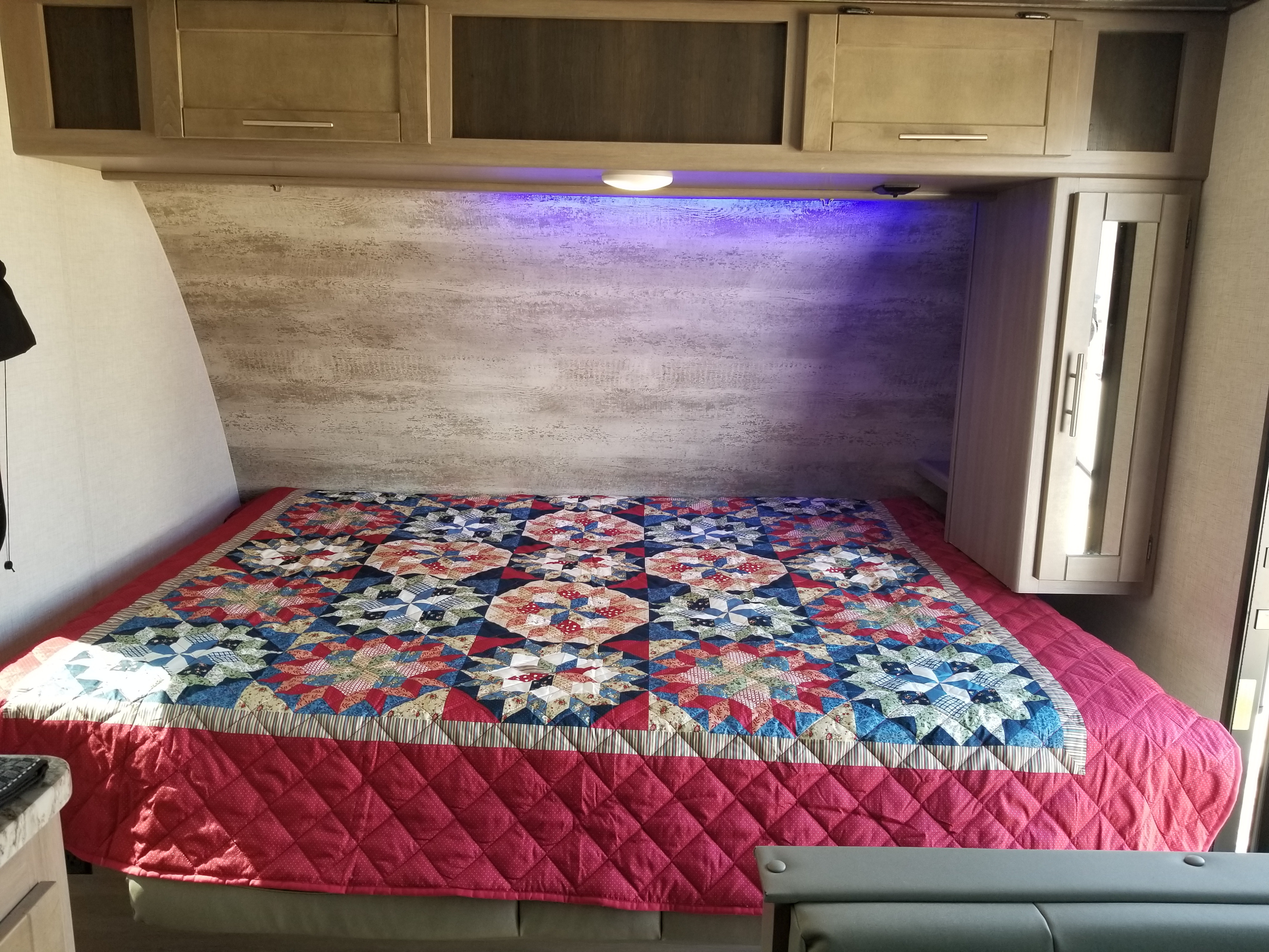 Cozy RV rental bedroom with a colorful quilt on the bed, wooden cabinets, and blue accent lighting.. Crossroads RV Sunset Trail Super Lite 2021