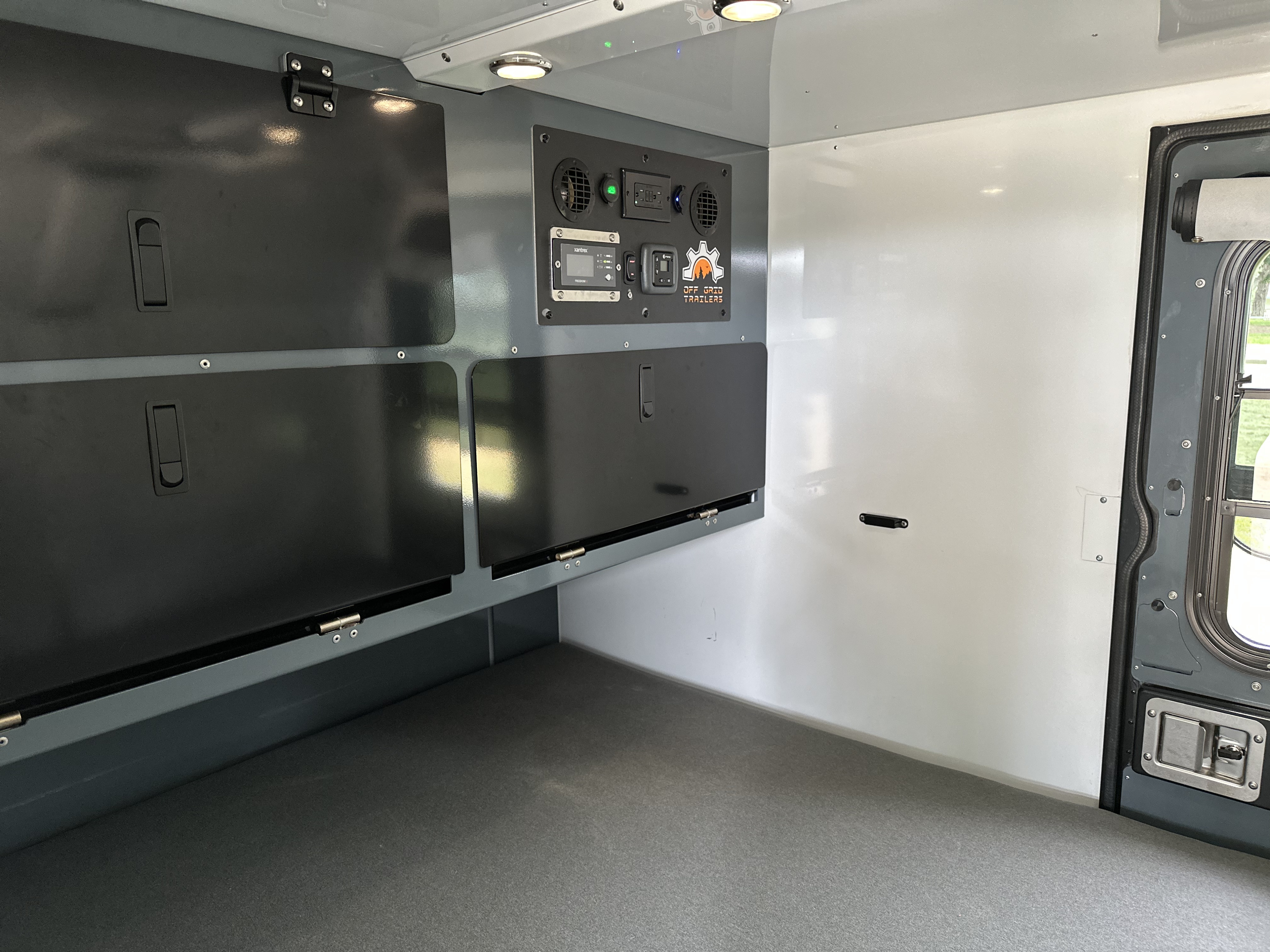 Inside an RV rental: off-grid trailer with integrated control panel, overhead lighting, and storage.. Off Grid Trailers Expedition 2022