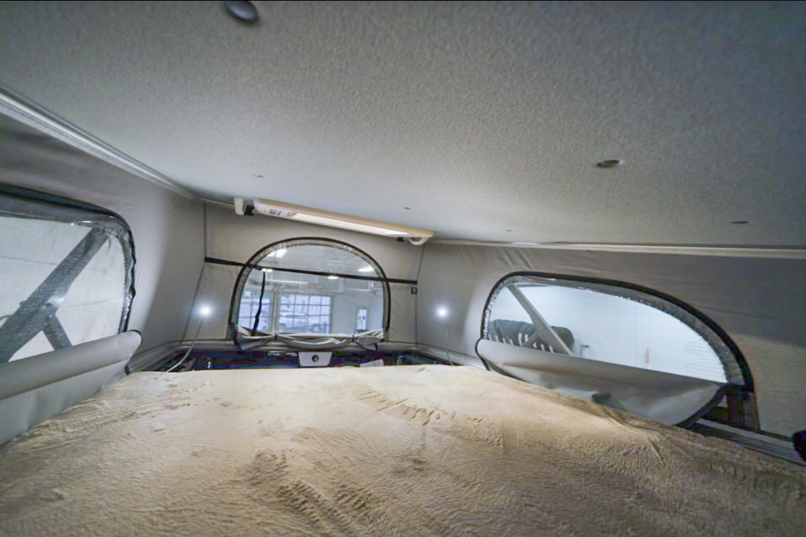 Spacious pop-top RV rental interior with a cozy bed, perfect for your next road trip adventure. Features large windows.. Thor Scope 18T 2021