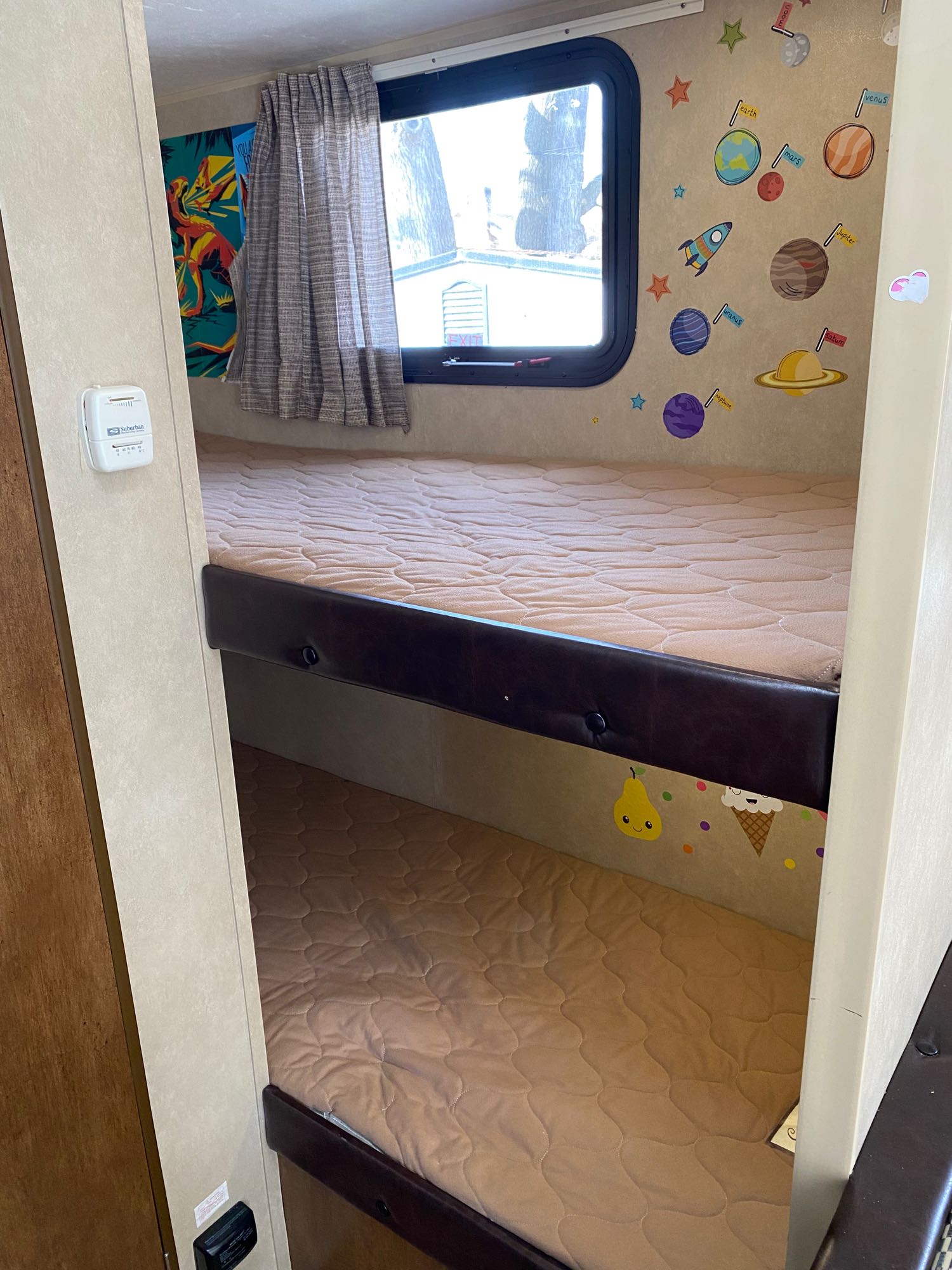 Inside an RV rental, two cozy bunk beds with quilted mattresses. Walls feature fun space & fruit decals. A window is by the top bunk.. Forest River Salem Cruise Lite 2016