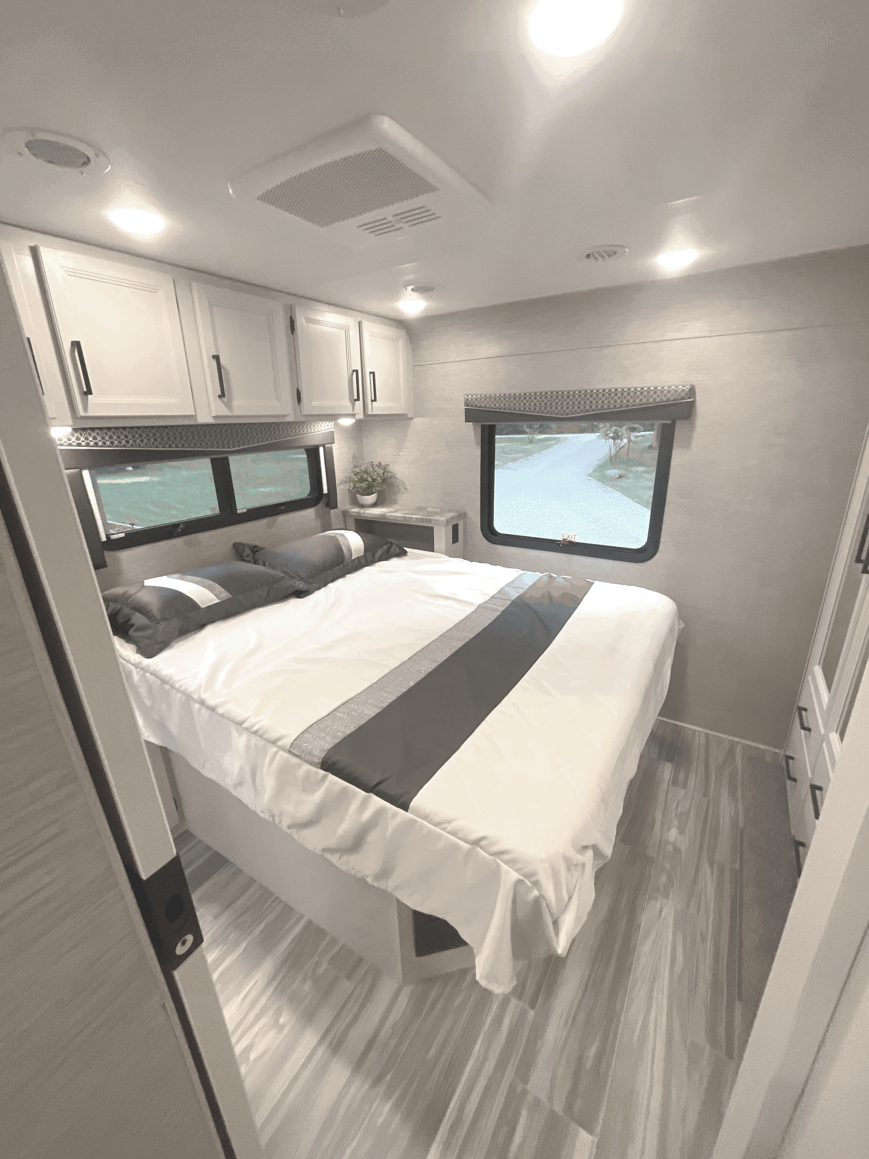 Bright RV rental bedroom features a comfy bed, overhead cabinets, and large windows with outdoor views.. Thor Four Winds 2022