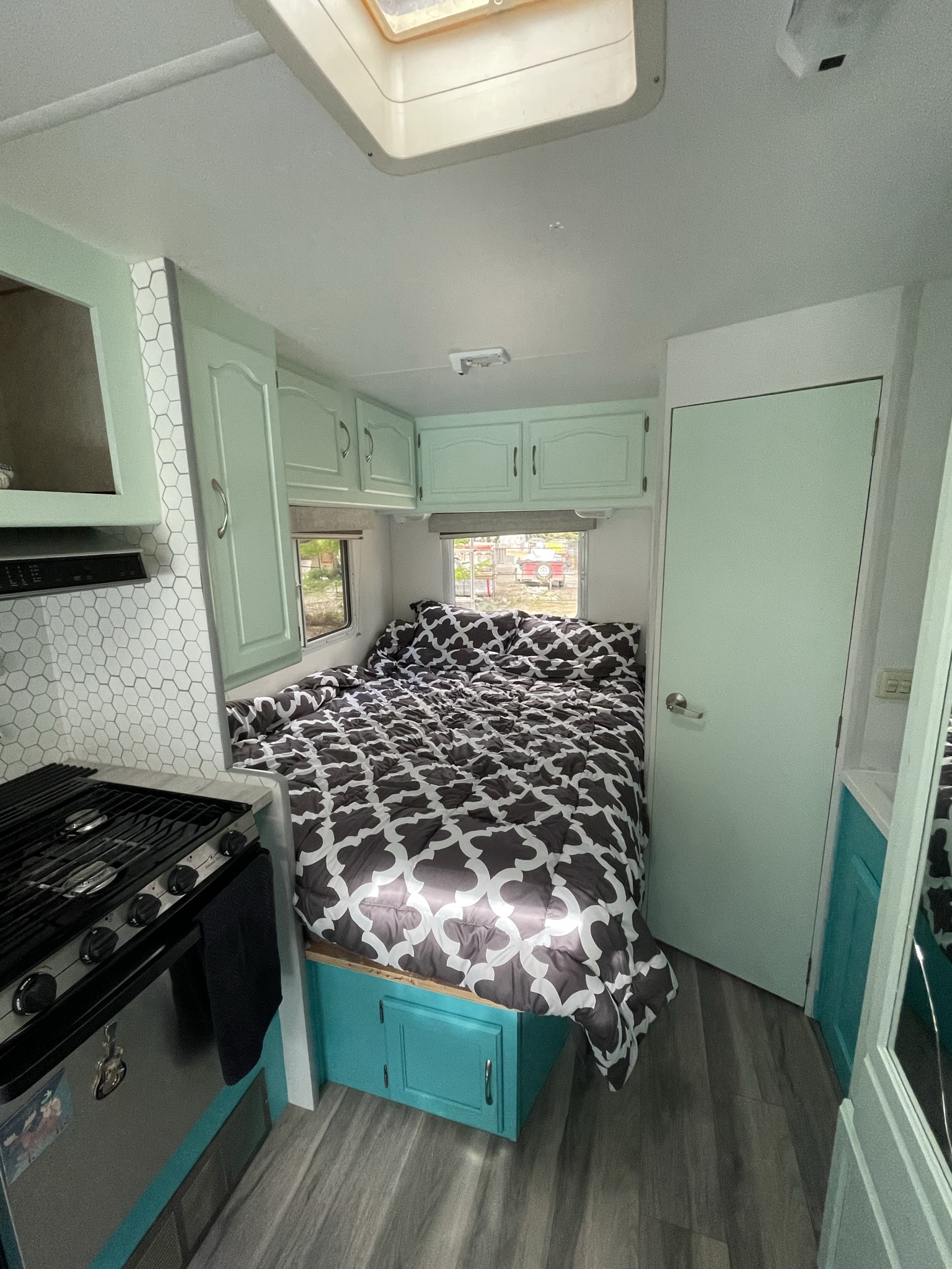 Bright RV rental interior: A bed with patterned comforter, mint green cabinets, and a white hexagon kitchen backsplash.. Other Other 2005
