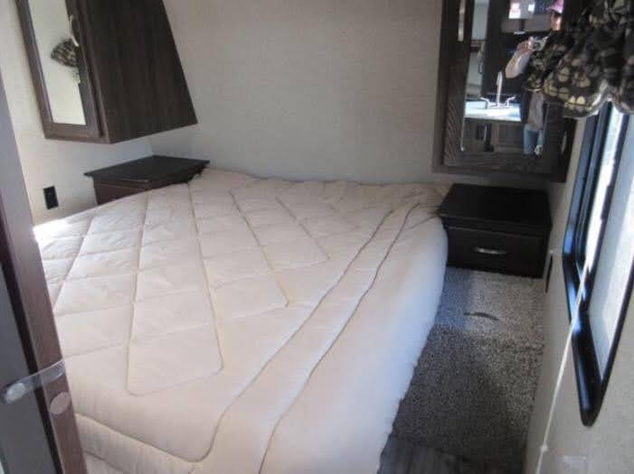 This RV rental bedroom features a comfy white quilted bed, dark nightstands, and mirrored wall cabinets, offering a cozy space for travel.. Keystone RV Springdale 2019