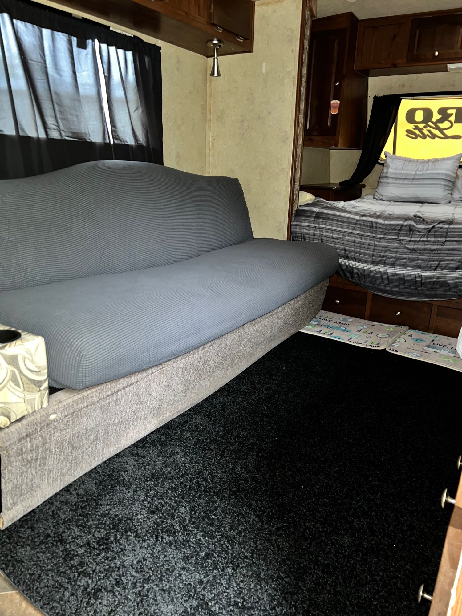 Cozy RV rental interior: grey futon, black carpet, and a comfortable bedroom area with striped bedding.. Forest River Flagstaff Micro Lite 2012