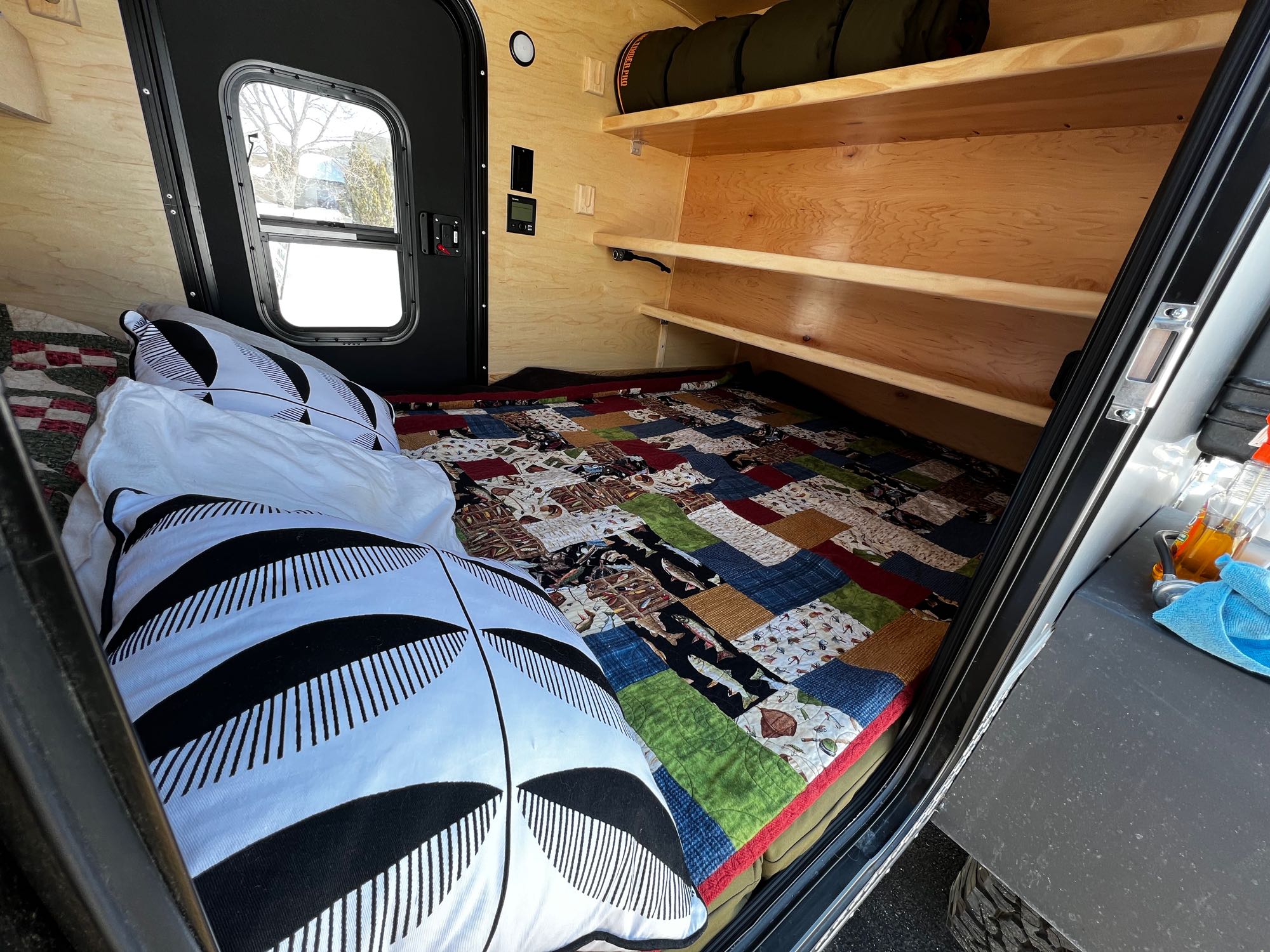 Cozy RV rental interior: bed with patchwork quilt, wood shelves, and window for a comfortable camping experience.. Colorado Teardrop Trailer Summit 2022