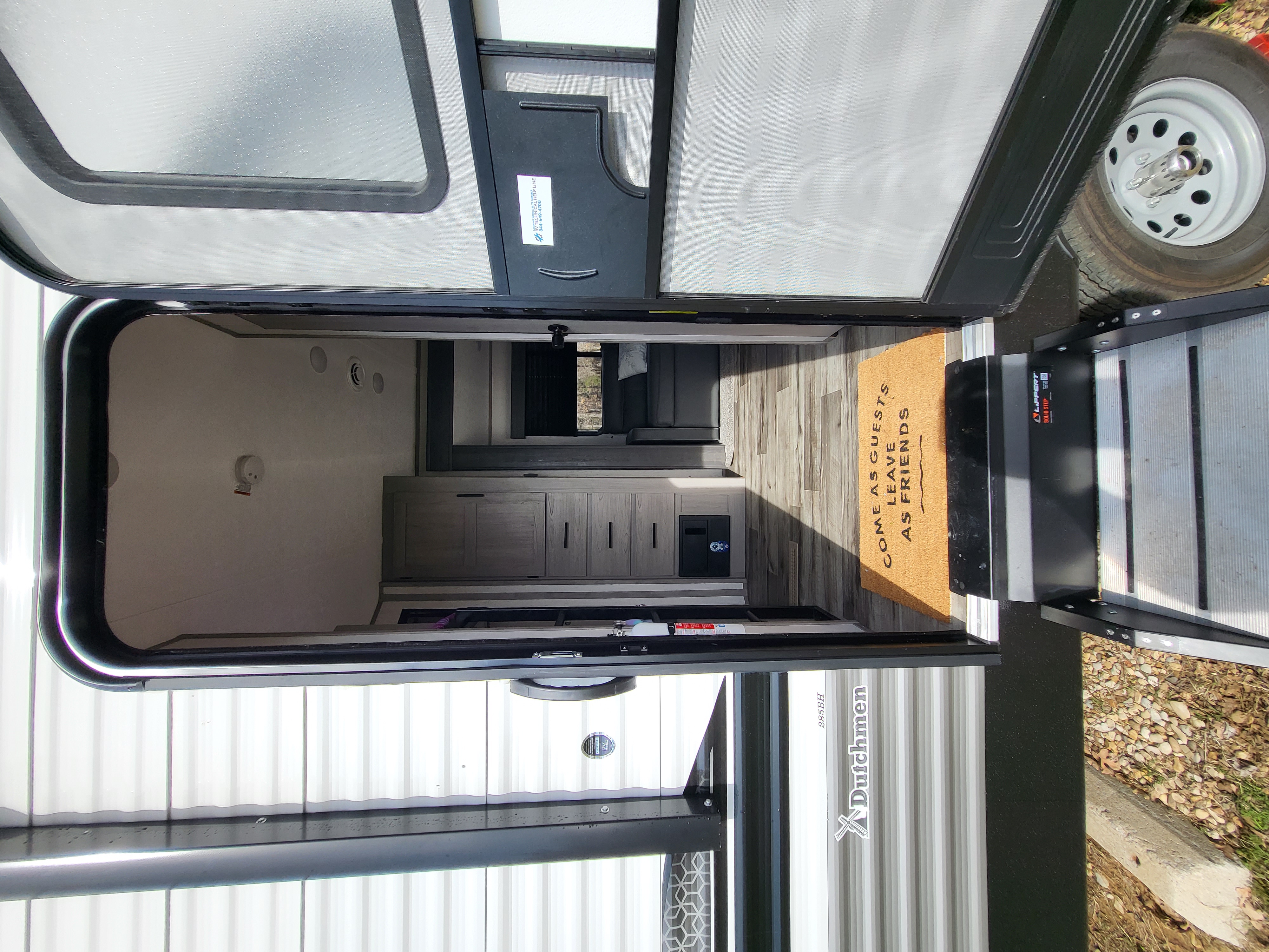 View inside an RV rental showing the inviting interior, 'COME AS GUESTS' doormat, and durable steps. Perfect for travel!. Dutchmen 285BH 2022