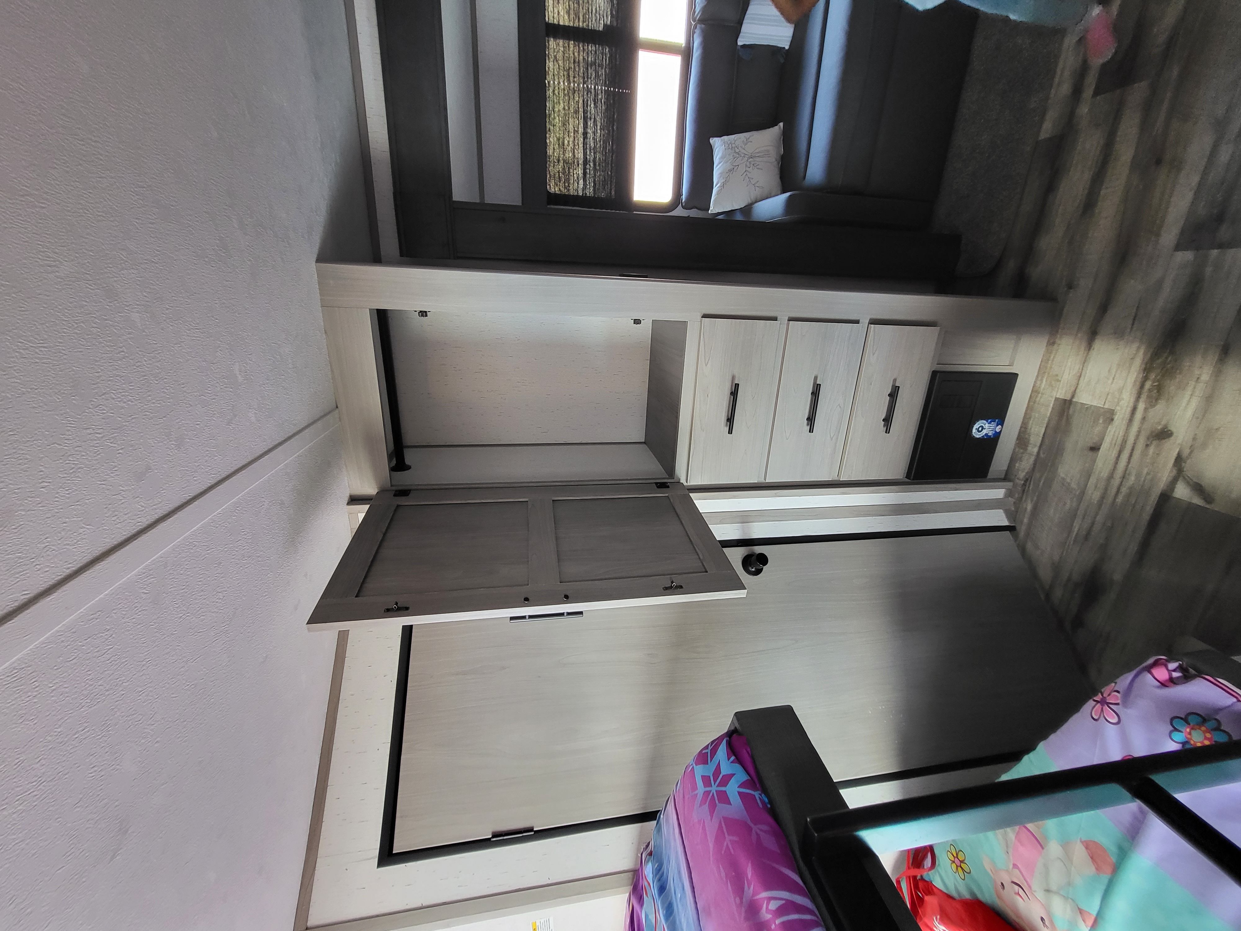 RV rental interior: light wood cabinets, sofa, window with blinds, and bunk area with colorful bedding. Practical and bright space.. Dutchmen 285BH 2022