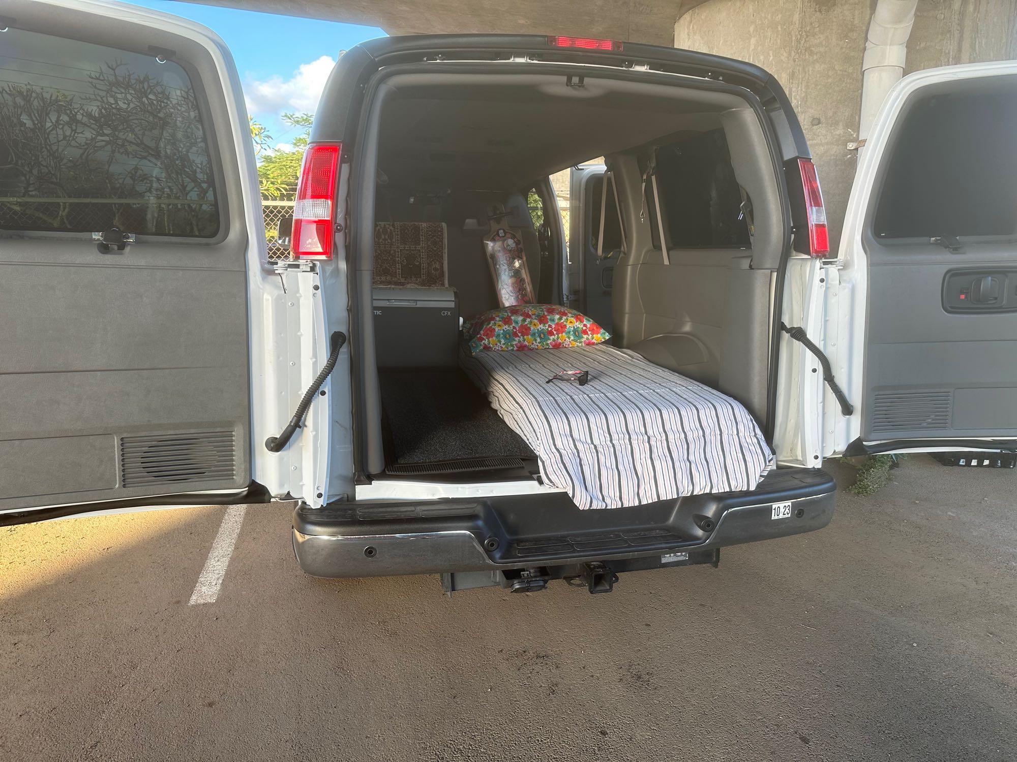 RV rental: White camper van with rear doors open, revealing a cozy bed and cooler setup for travel.. Chevrolet Other 2022