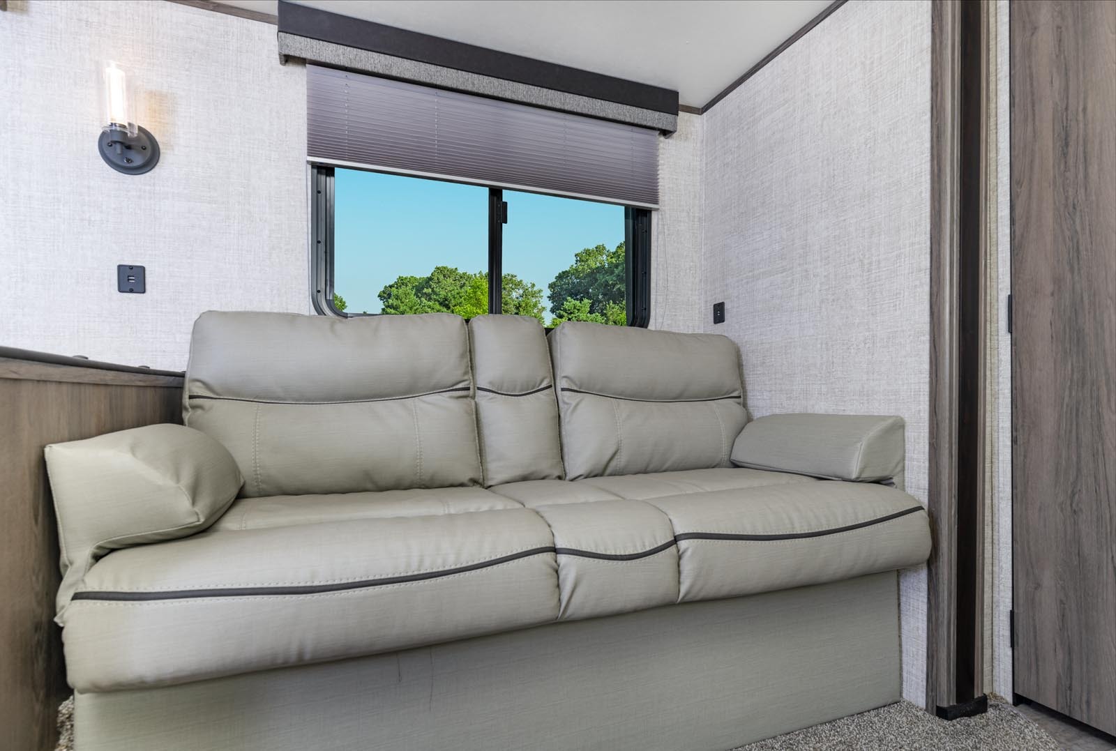 Inside this RV rental, a light gray sofa bed sits by a window with a green outdoor view, offering comfort and relaxation.. Gulf Stream 268BHS 2023