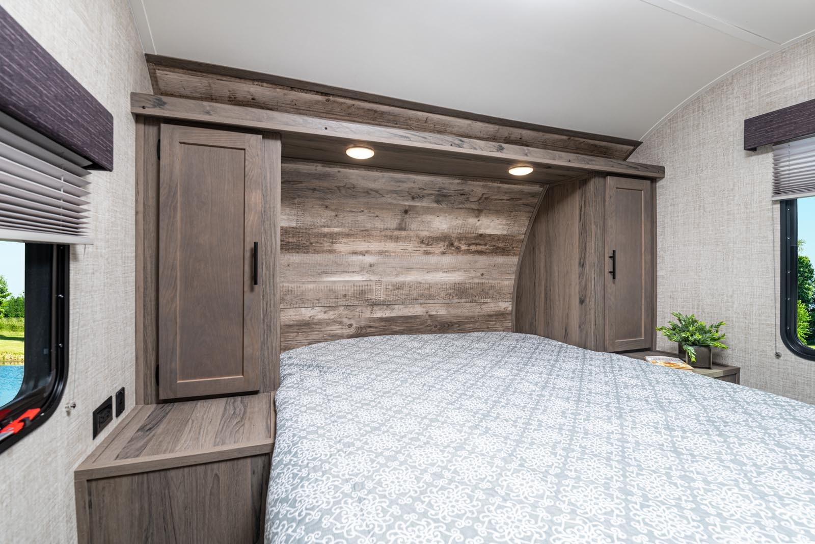 Cozy RV rental bedroom features rustic wood-look headboard, lighting, storage, and a scenic window view.. Gulf Stream 268BHS 2023