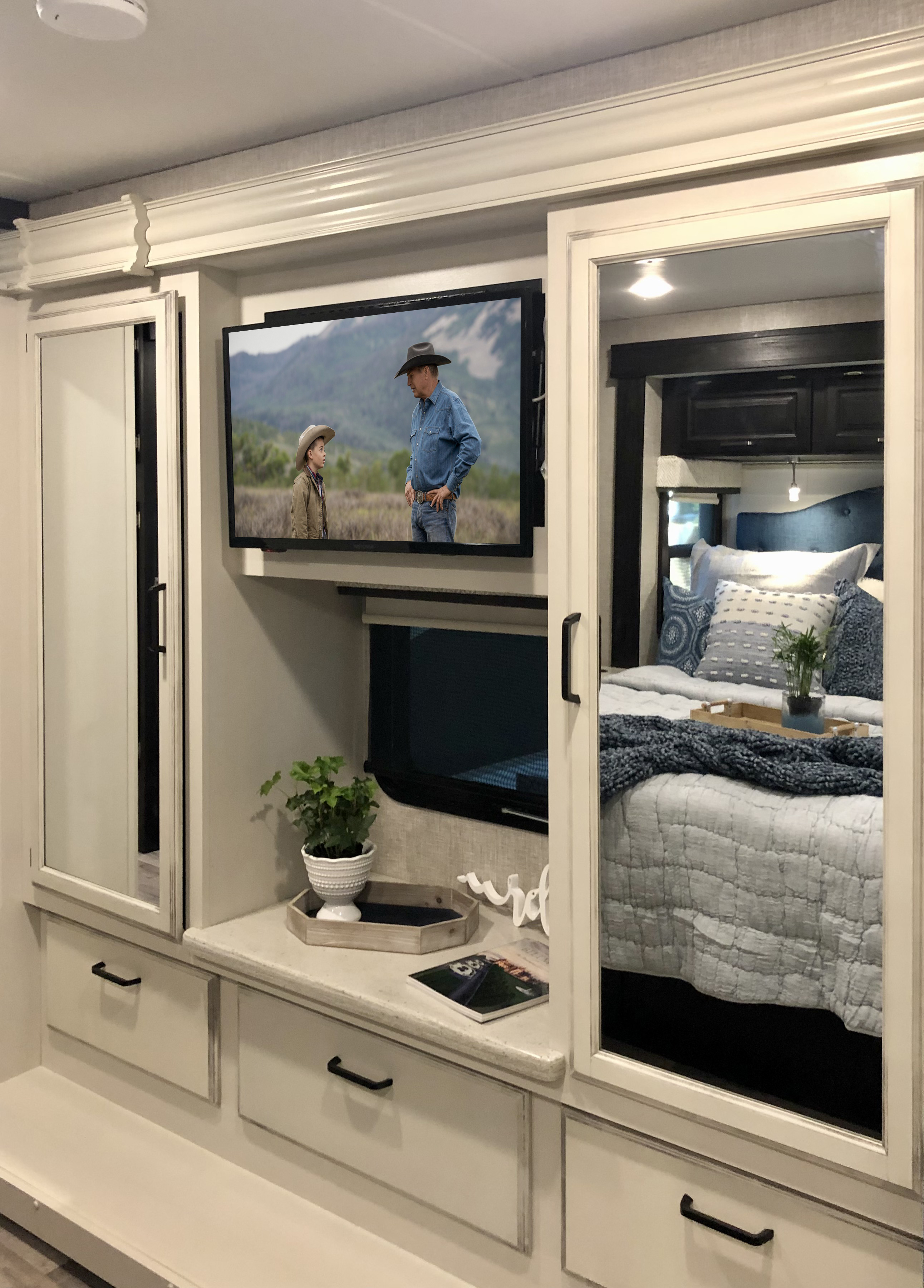 Inside a modern RV rental: a bedroom with a TV showing Yellowstone, mirrored wardrobe doors, and practical drawer storage.. Jayco Precept 2023