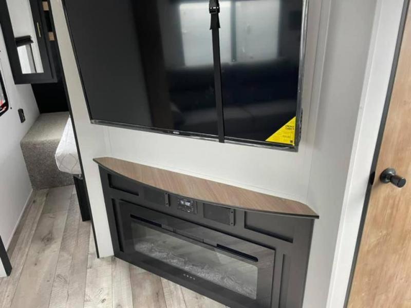 Modern RV rental interior with a flat-screen TV over an electric fireplace, next to a cozy bed nook.. Keystone RV Springdale 2022