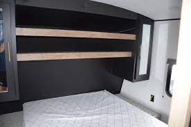 Inside an RV rental bedroom, featuring a mattress, dark wall-mounted shelves, and mirrored cabinets for organized storage.. Keystone RV Springdale 2022