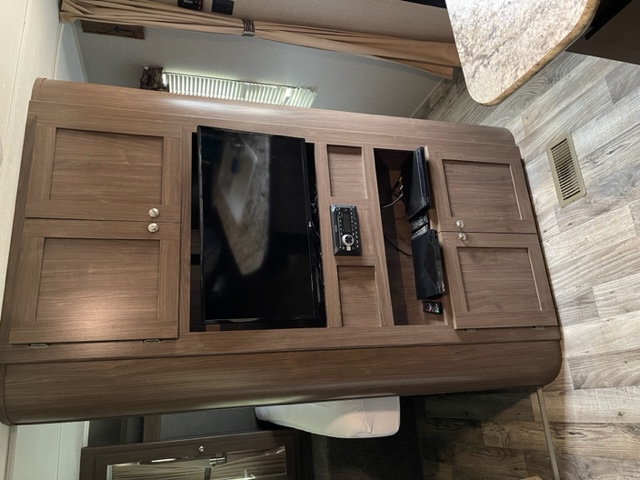 Inside an RV rental: A central wooden entertainment unit with a TV, stereo, and storage cabinets.. Keystone Hideout 2019