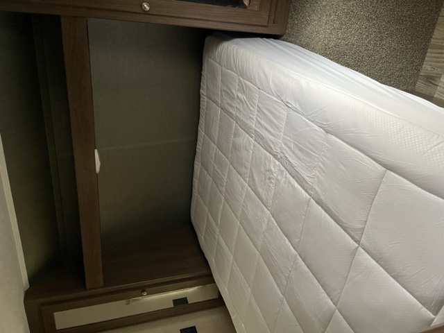 RV rental compact sleeping area: a comfortable bed with white mattress and adjacent built-in closet storage, perfect for travel.. Keystone Hideout 2019