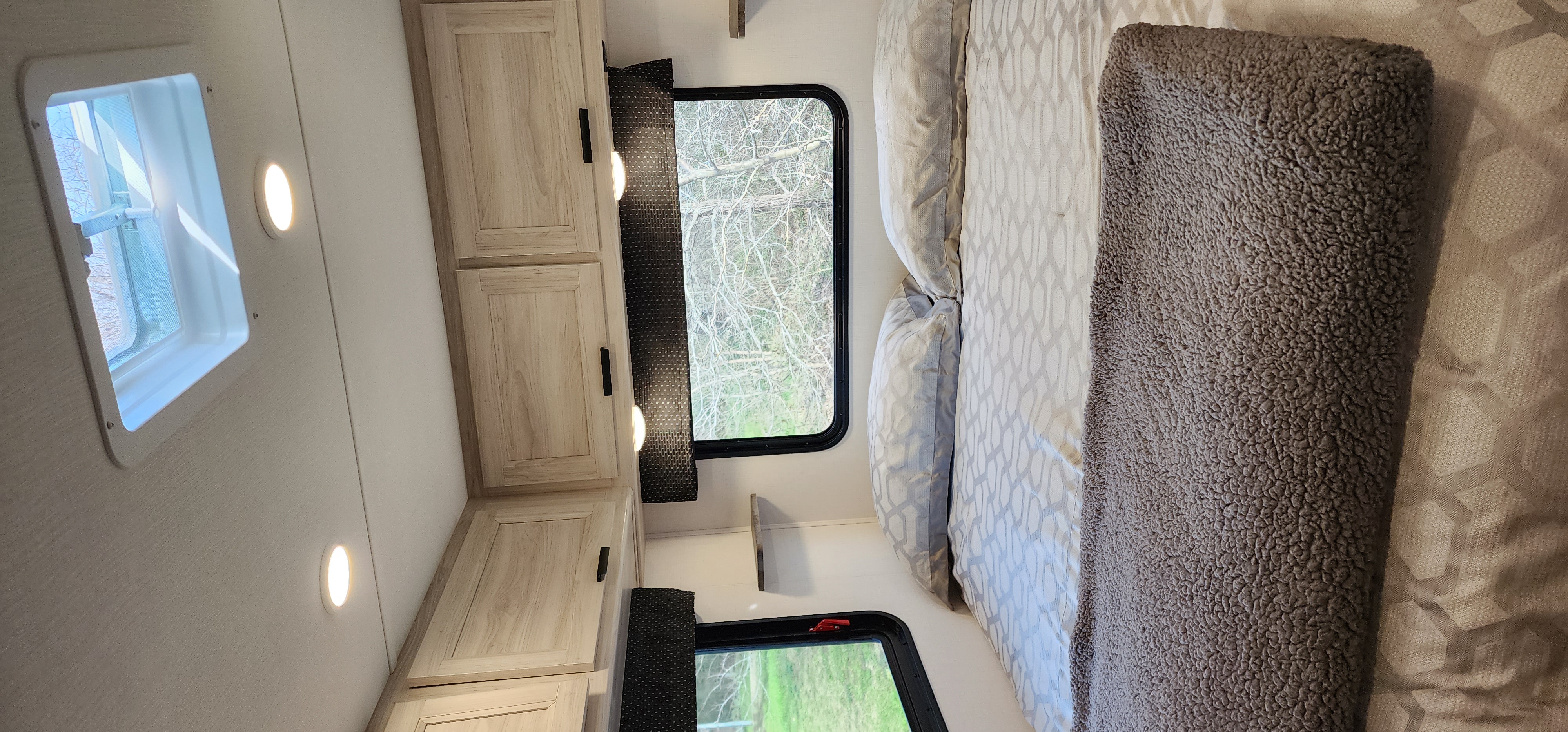 Inside a comfy RV rental bedroom: light wood cabinets, bright windows, and a bed with patterned linens & fuzzy blanket.. Forester LE 2022