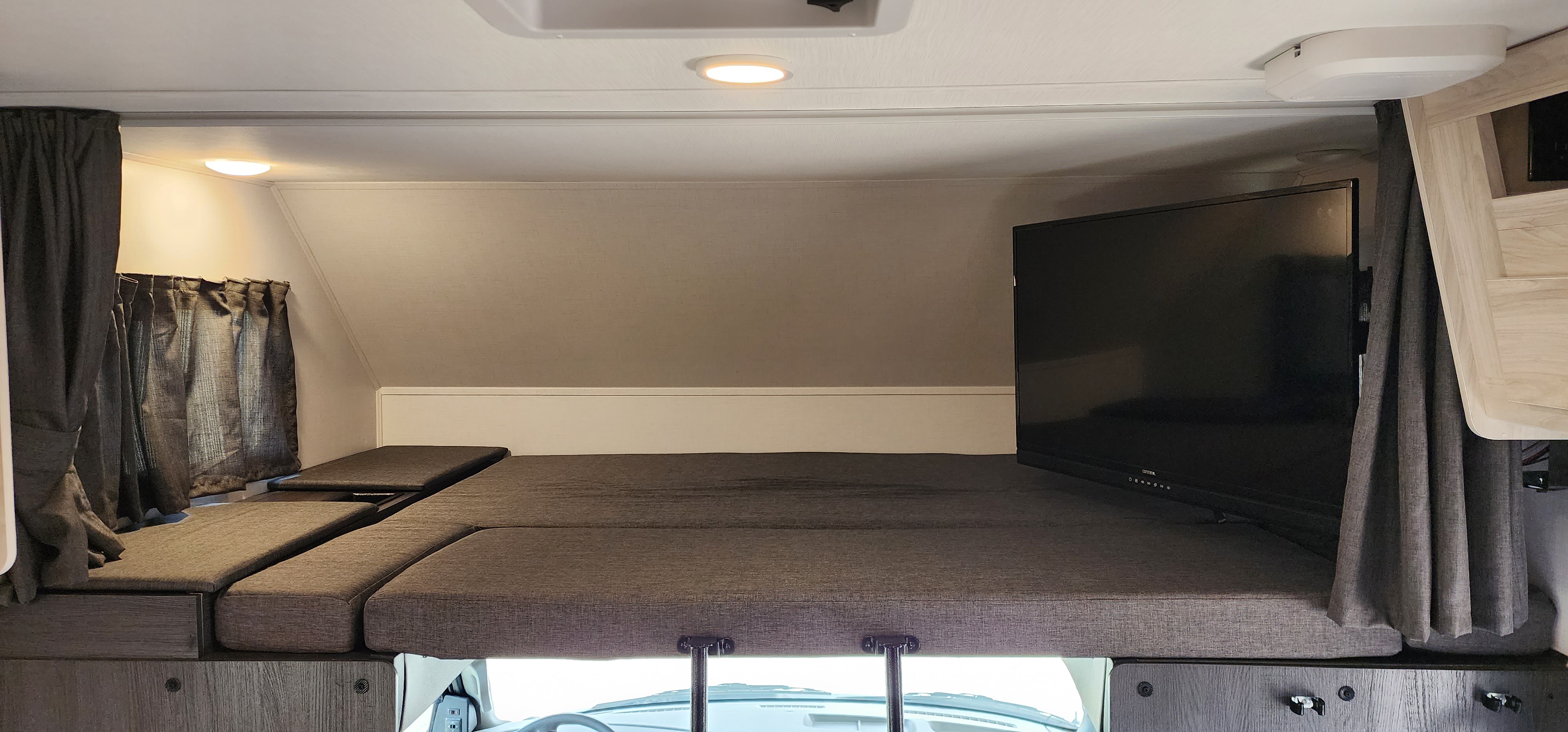 RV rental over-cab sleeping area with gray bed cushions, mounted TV, and privacy curtains for comfortable travel.. Forester LE 2022