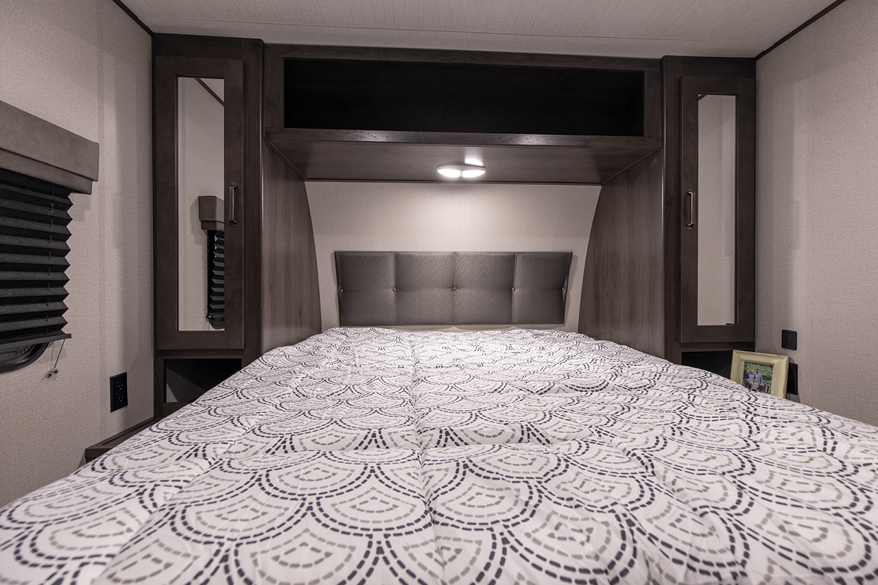 Cozy RV rental bedroom featuring a patterned bed, padded headboard, and built-in storage, perfect for comfortable travel.. Grand Design Transcend Xplor 265BH 2022