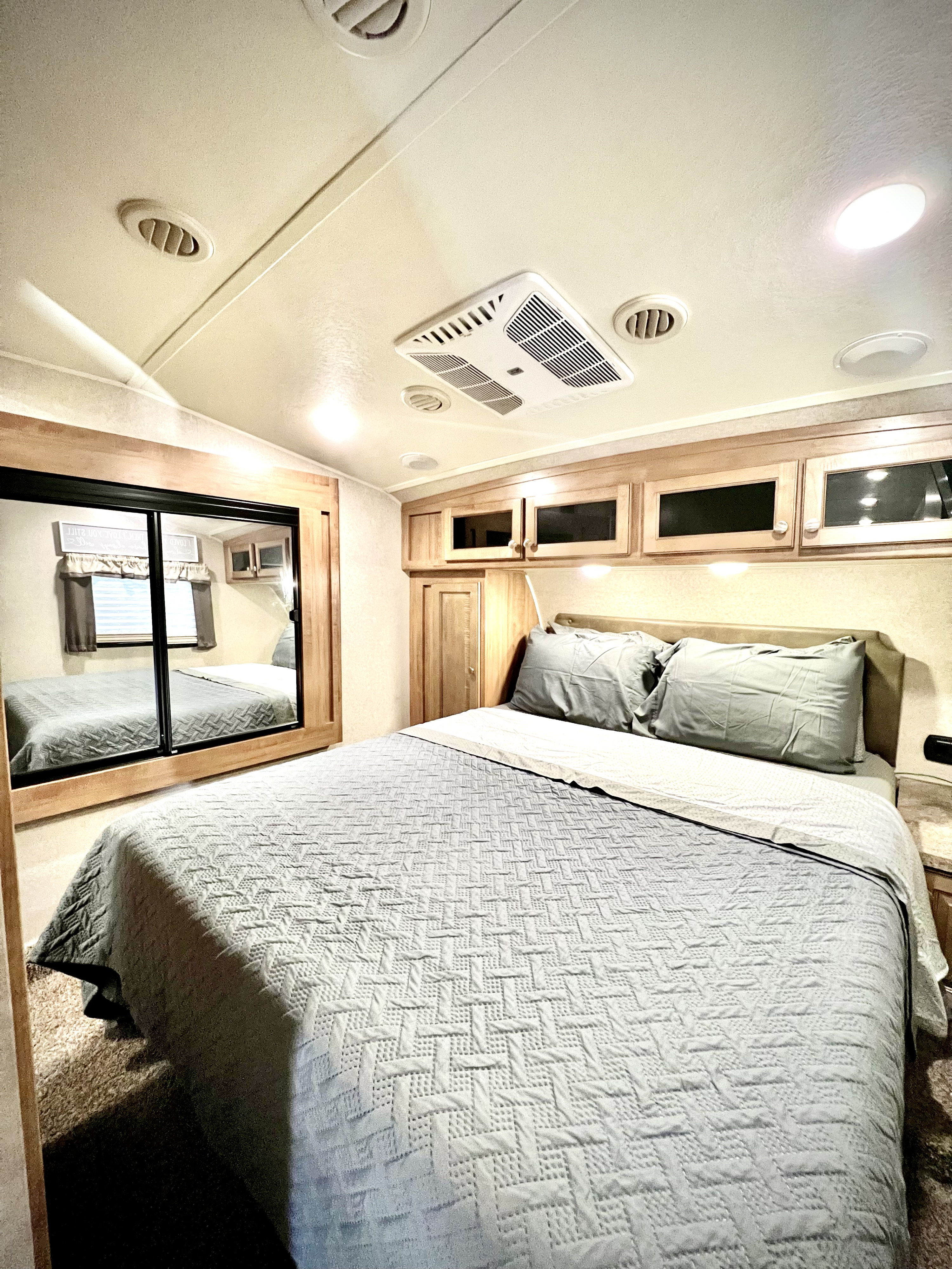 RV rental bedroom featuring a grey bed, mirrored closet, overhead storage, and AC for comfortable travel.. Forest River Flagstaff 2018