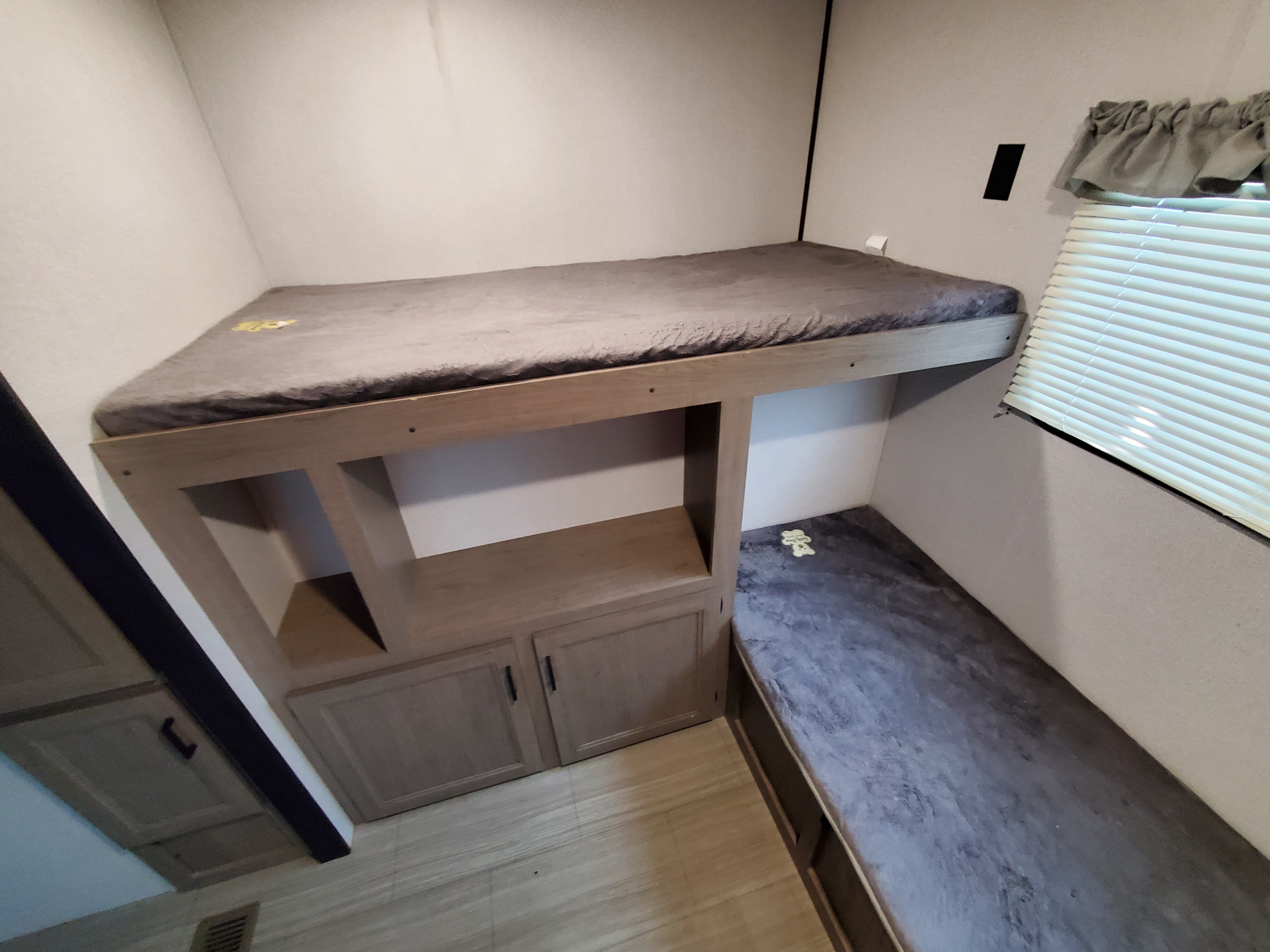 This cozy RV rental bunk area features an upper bunk, a lower bench/bed, built-in storage cabinets, and a window with blinds.. Keystone Hideout 2020