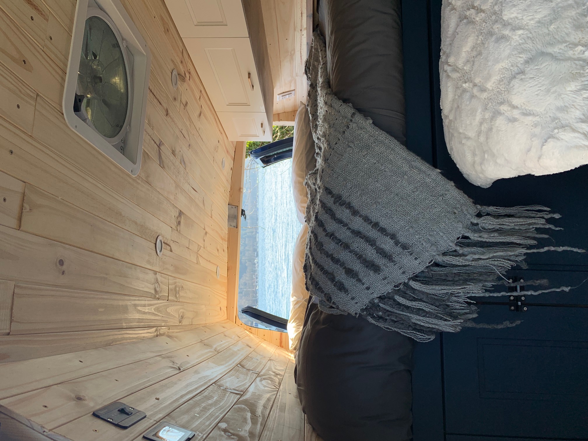 RV rental interior: wood-paneled walls, ceiling fan, cozy bed, and tranquil water view from the rear.. Ford E350 Box Van 2010