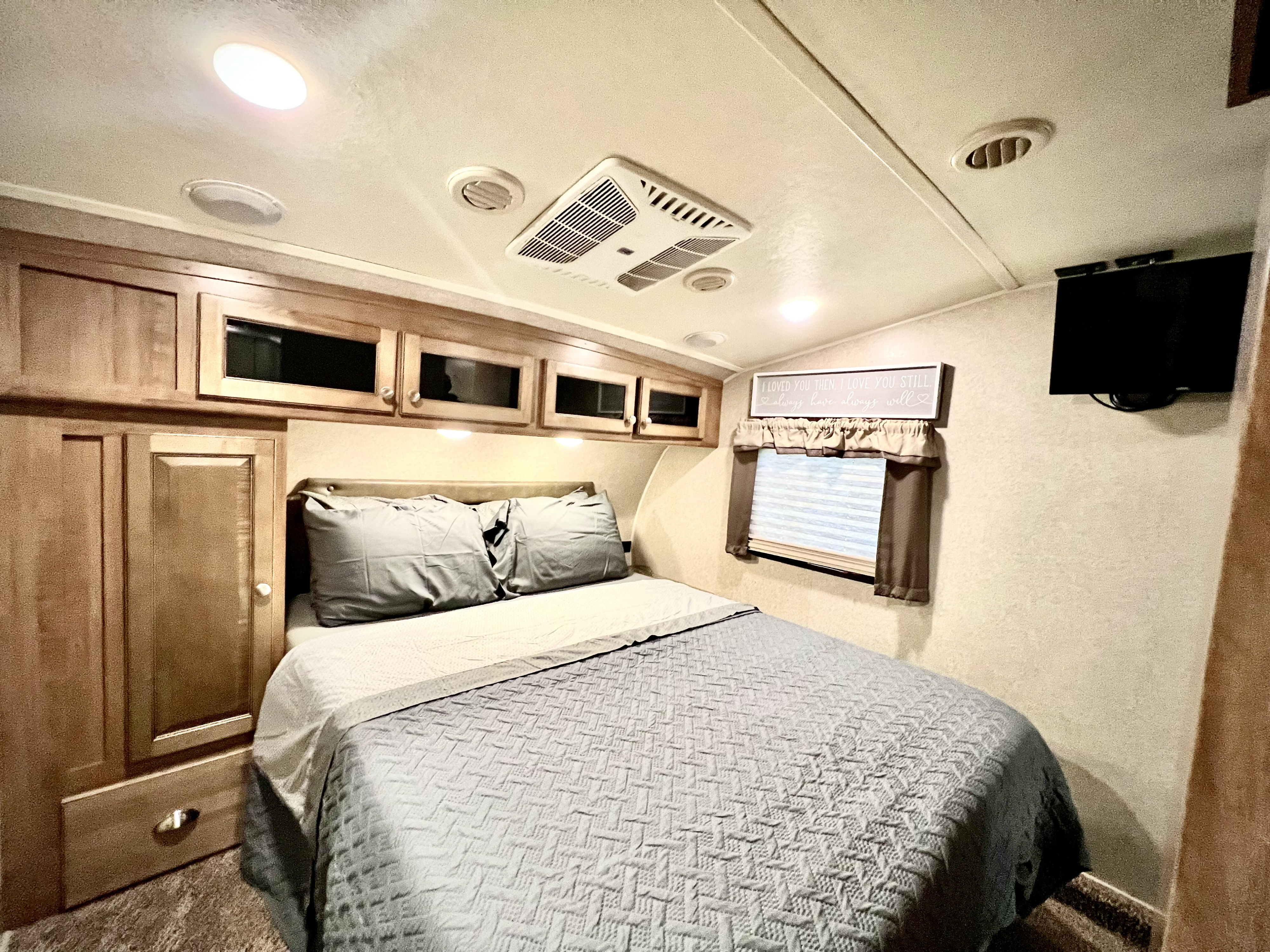 Step into comfort: This RV rental bedroom features a cozy bed, wood cabinets, TV, and a window for a relaxing stay.. Forest River Flagstaff 2018
